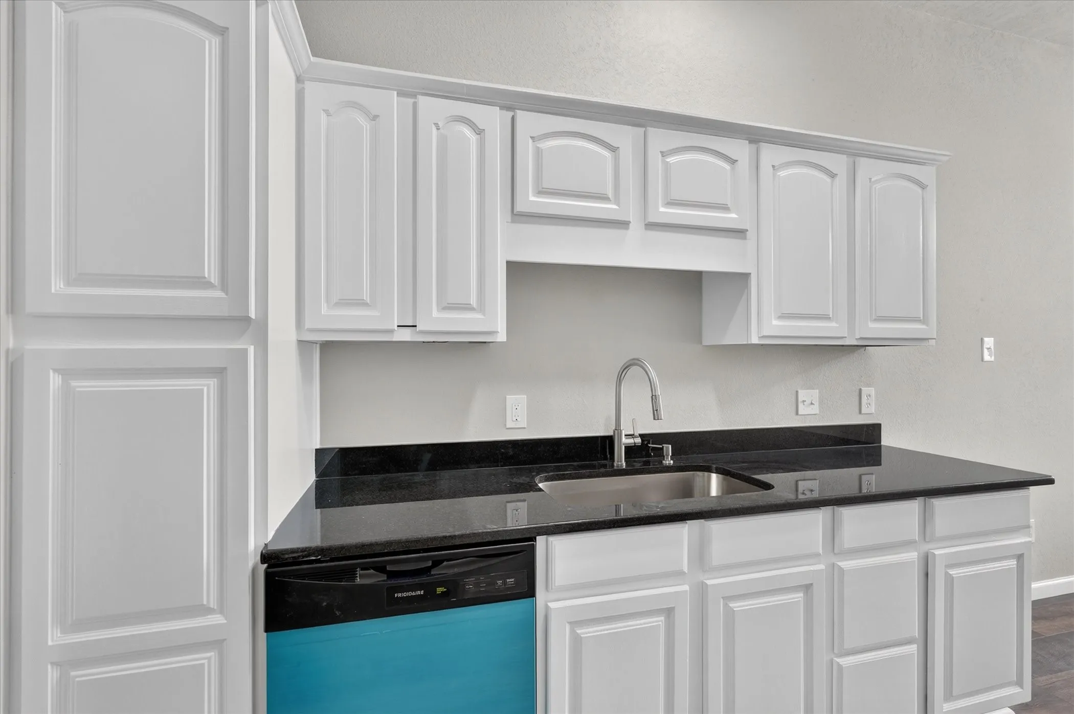 White cabinetry with crown molding, black countertops, stainless steel sink, and a high-arc faucet