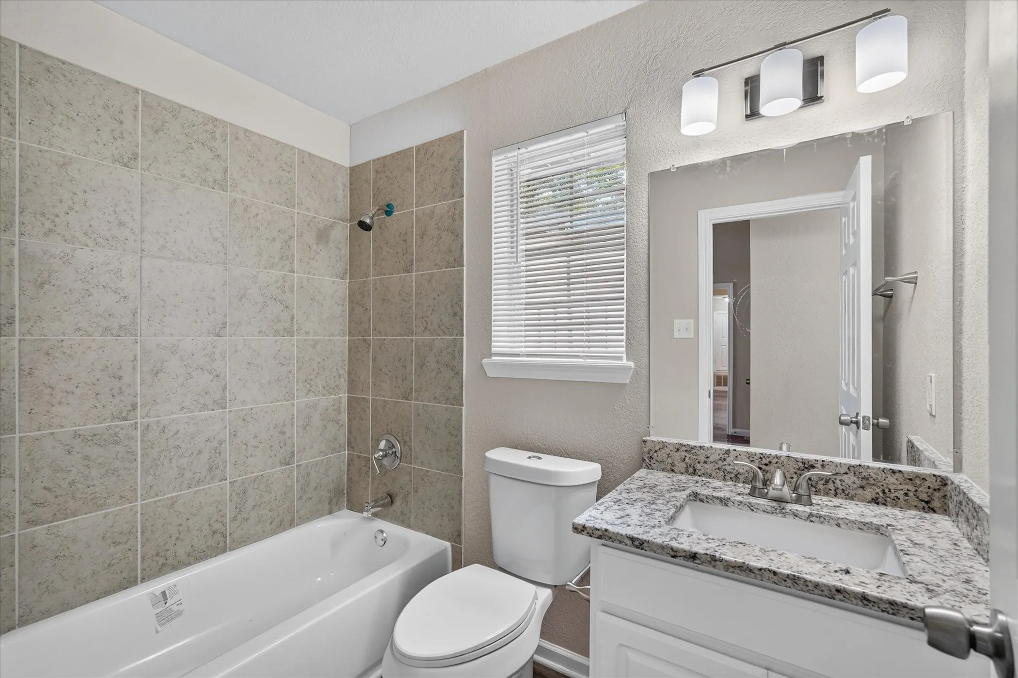 Bathroom featuring a tiled shower surround, white bathtub, vanity with a stone countertop, and an overhead light fixture