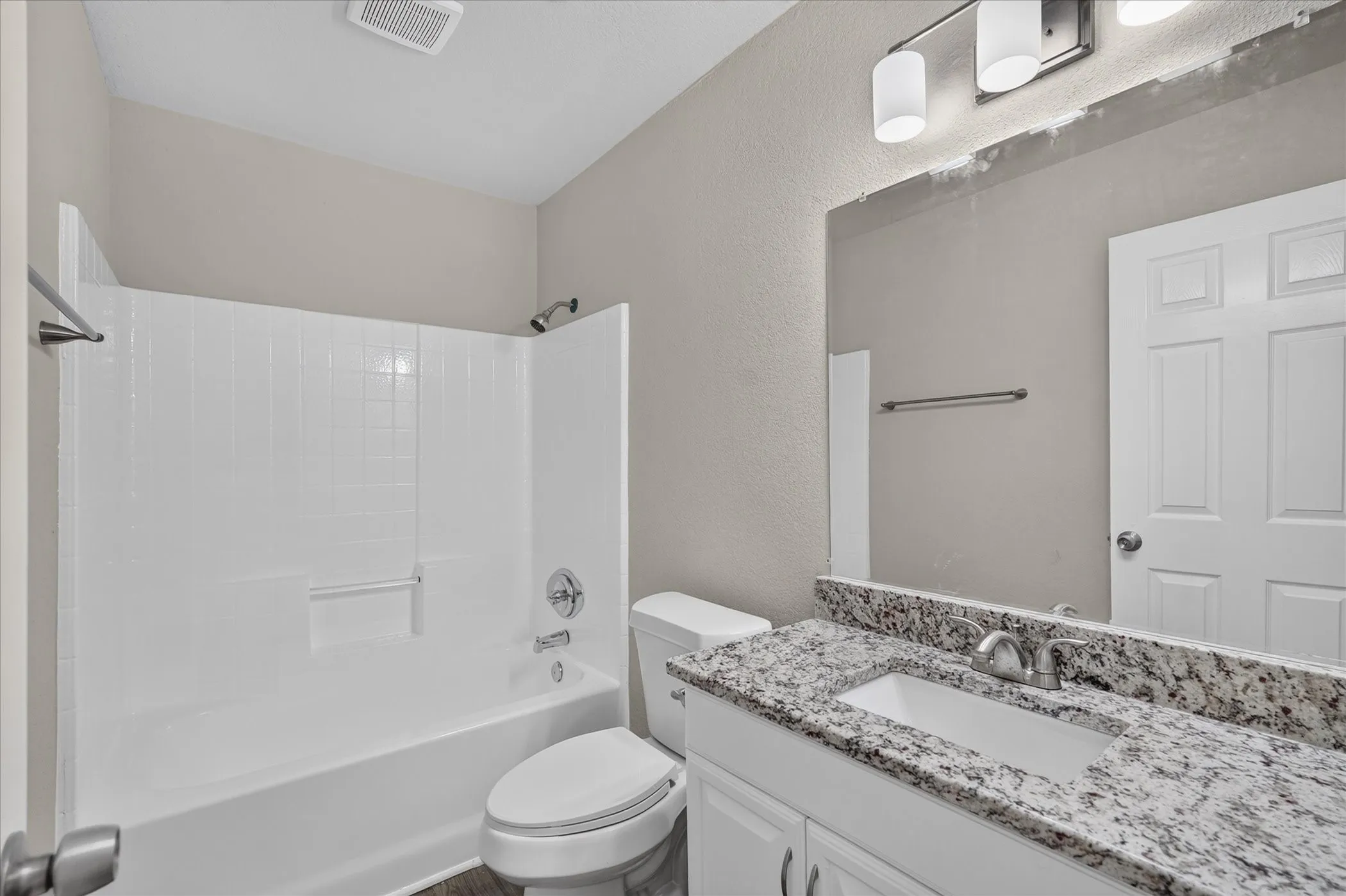 Tub and shower combination with chrome fixtures, vanity with a speckled countertop, and built-in white cabinetry