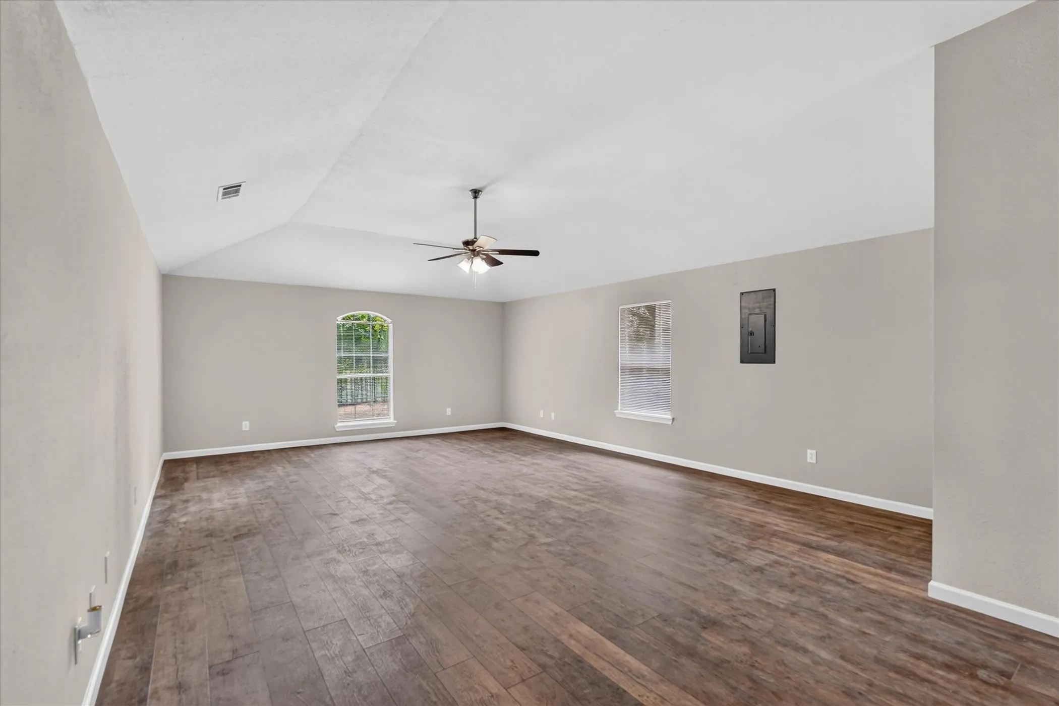 Vaulted ceiling, wood-finish flooring, ceiling fan, arched window, and neutral wall tones