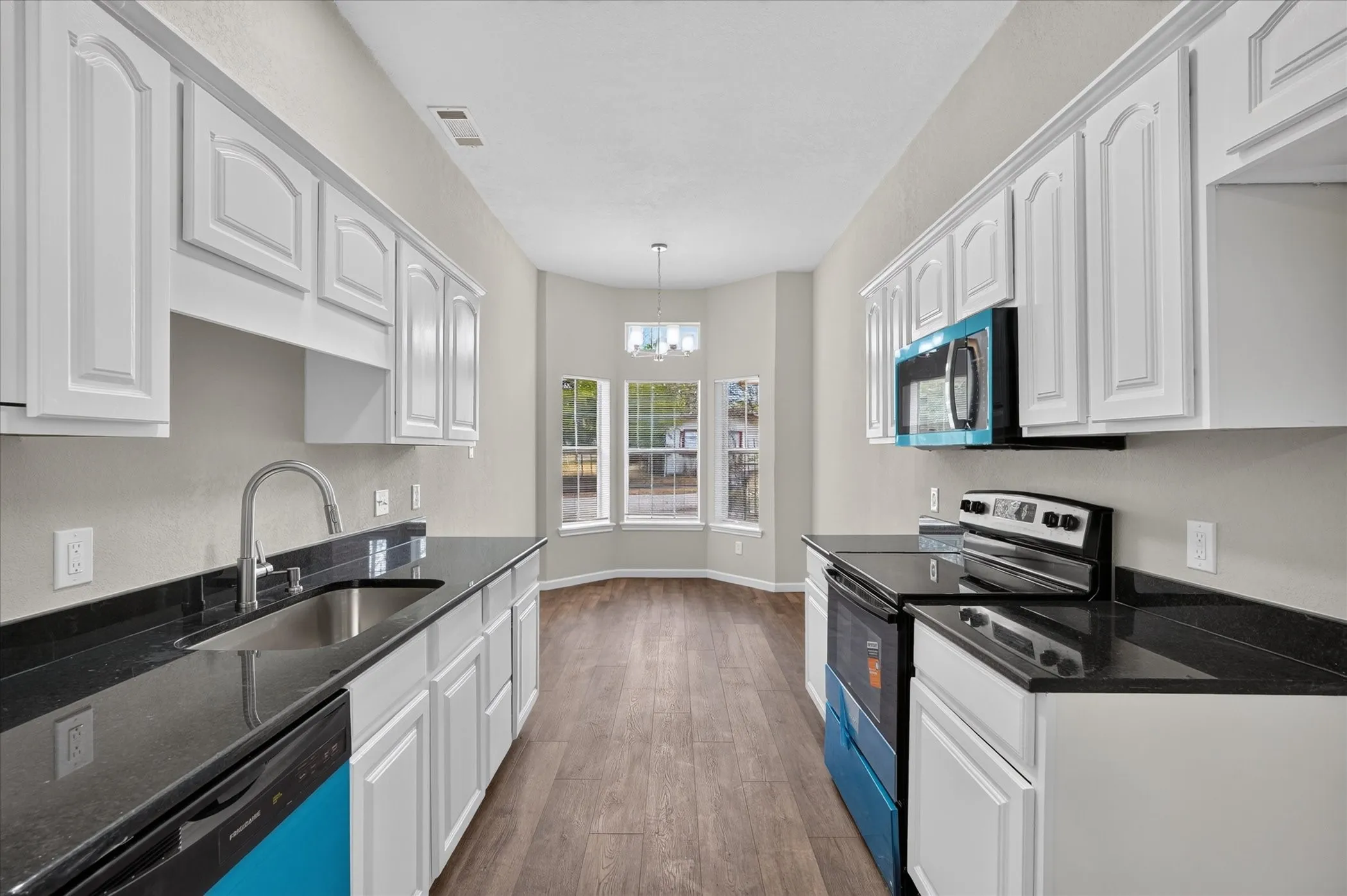Kitchen featuring white cabinetry, dark countertops, stainless steel sink, wood-finish flooring, and bay windows