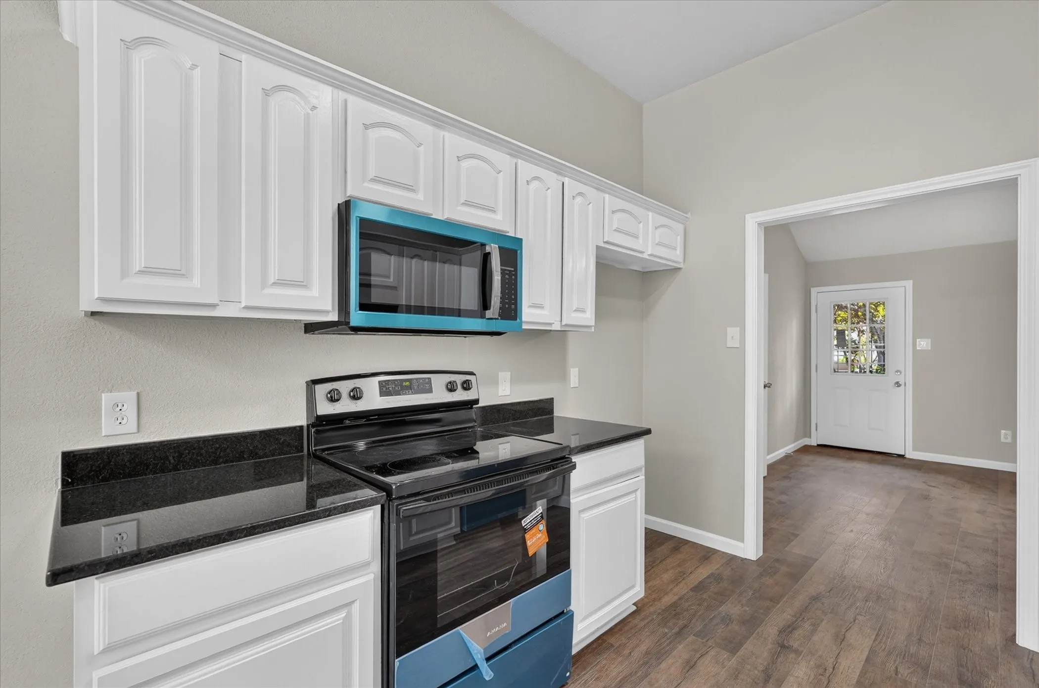 White cabinetry, dark countertops, wood-finish flooring, and a vaulted ceiling