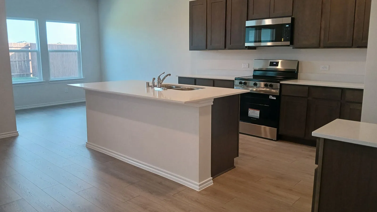 Modern kitchen with wood-finish flooring, dark wood cabinetry, white countertops, and stainless steel appliances