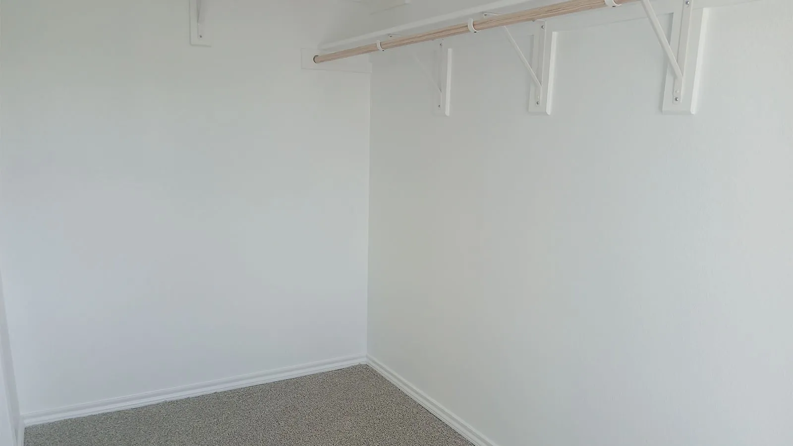White painted walls with gray carpet flooring and a wood-finish clothing rod