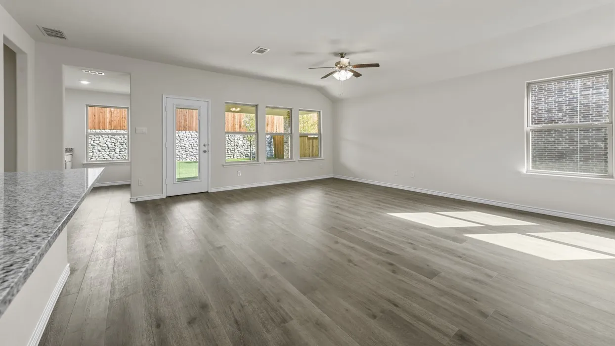 Spacious living area featuring contemporary wood-finish flooring, vaulted ceiling with a ceiling fan, and multiple windows providing natural illumination