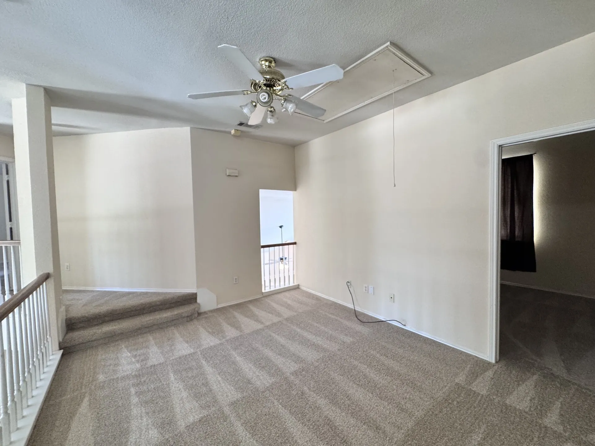 Carpeted open area with a ceiling fan, access panel, and a railing overlooking a lower level
