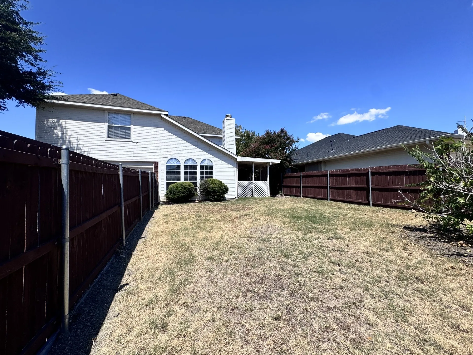 Expansive backyard featuring a privacy fence, white brick exterior, and arched window details
