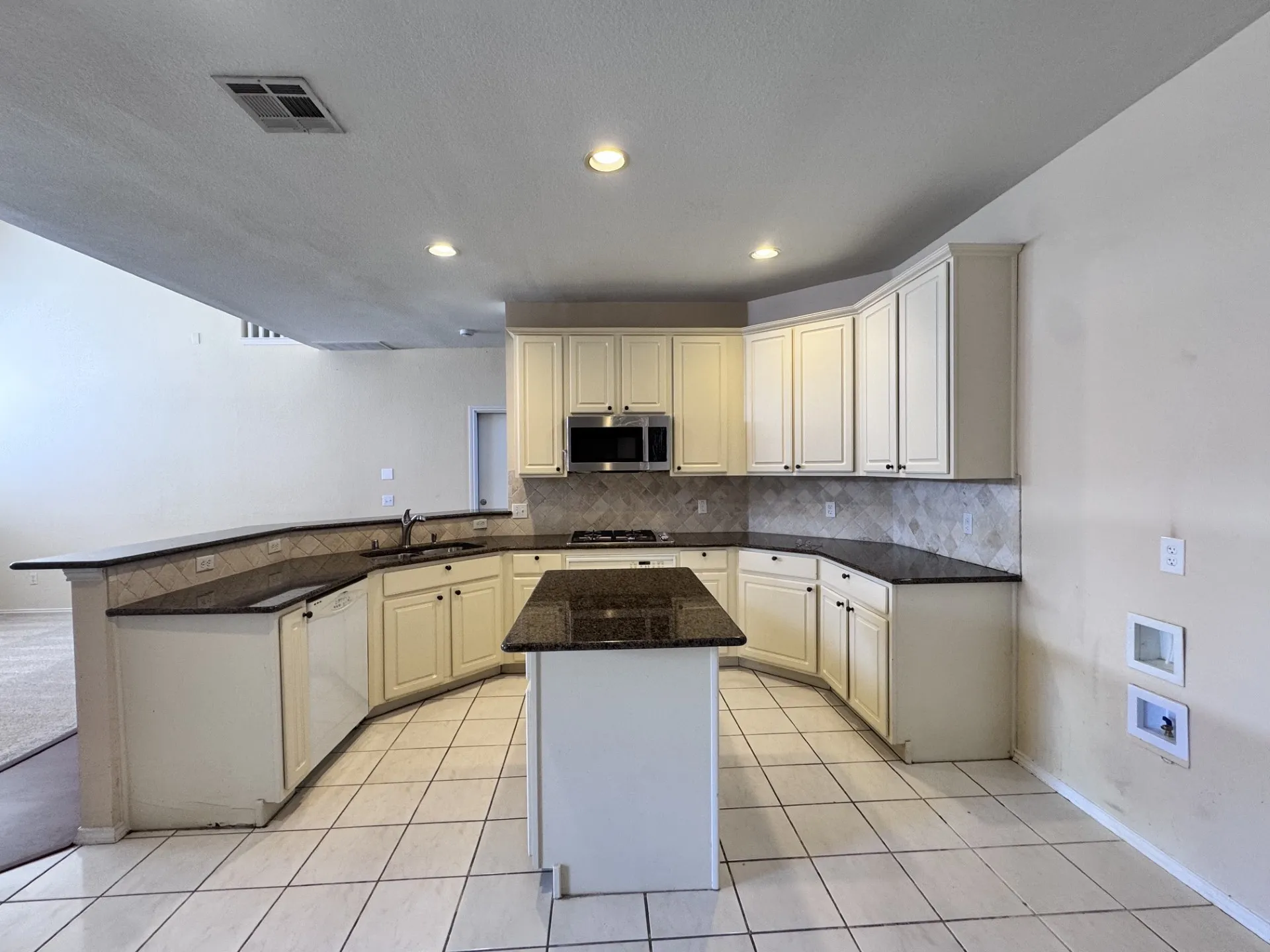 Kitchen featuring cream-colored cabinetry, dark countertops, a center island, recessed lighting, and a tile backsplash
