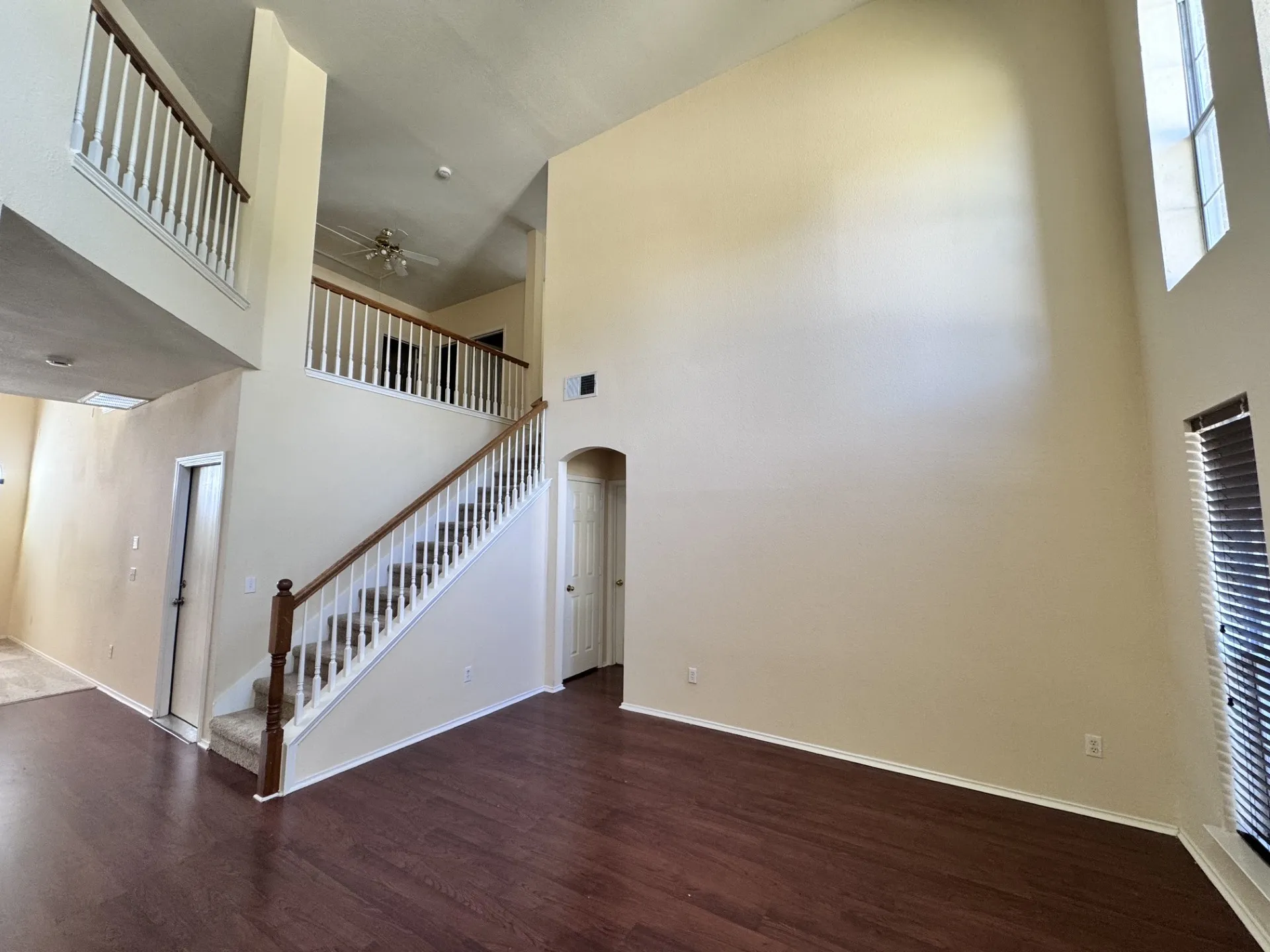Vaulted ceilings, wood-finish flooring, two-story windows, staircase with wood handrail, and an arched doorway