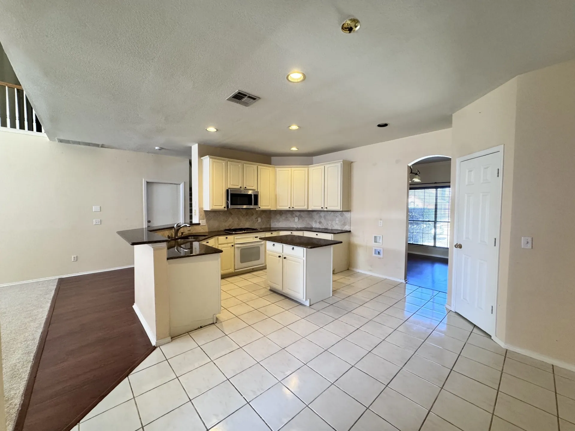 Open-concept kitchen with white cabinetry and dark countertops, featuring a central island and white tile flooring