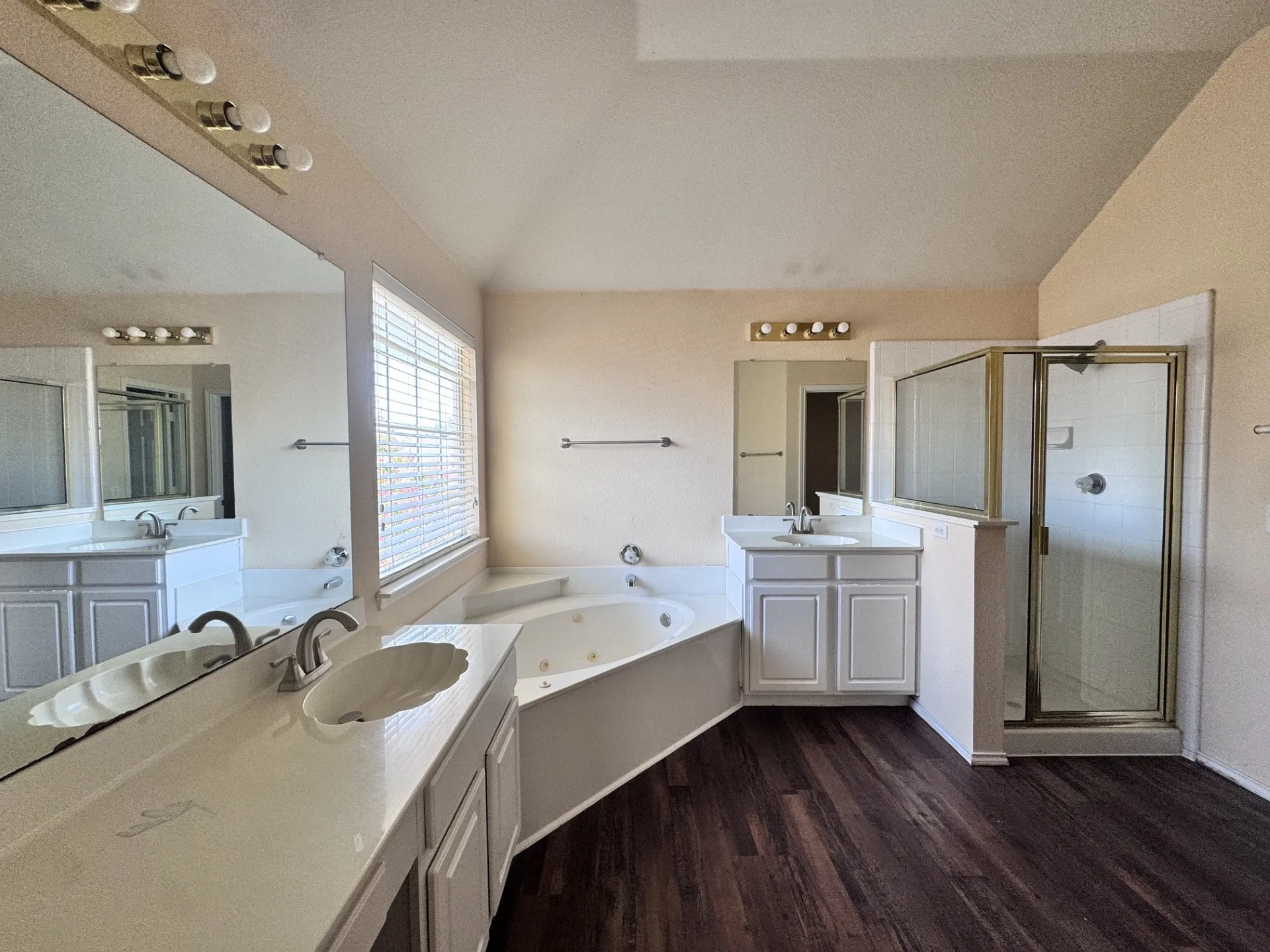 Dual vanity with integrated sinks, corner jetted tub, separate shower enclosure, and wood-finish flooring
