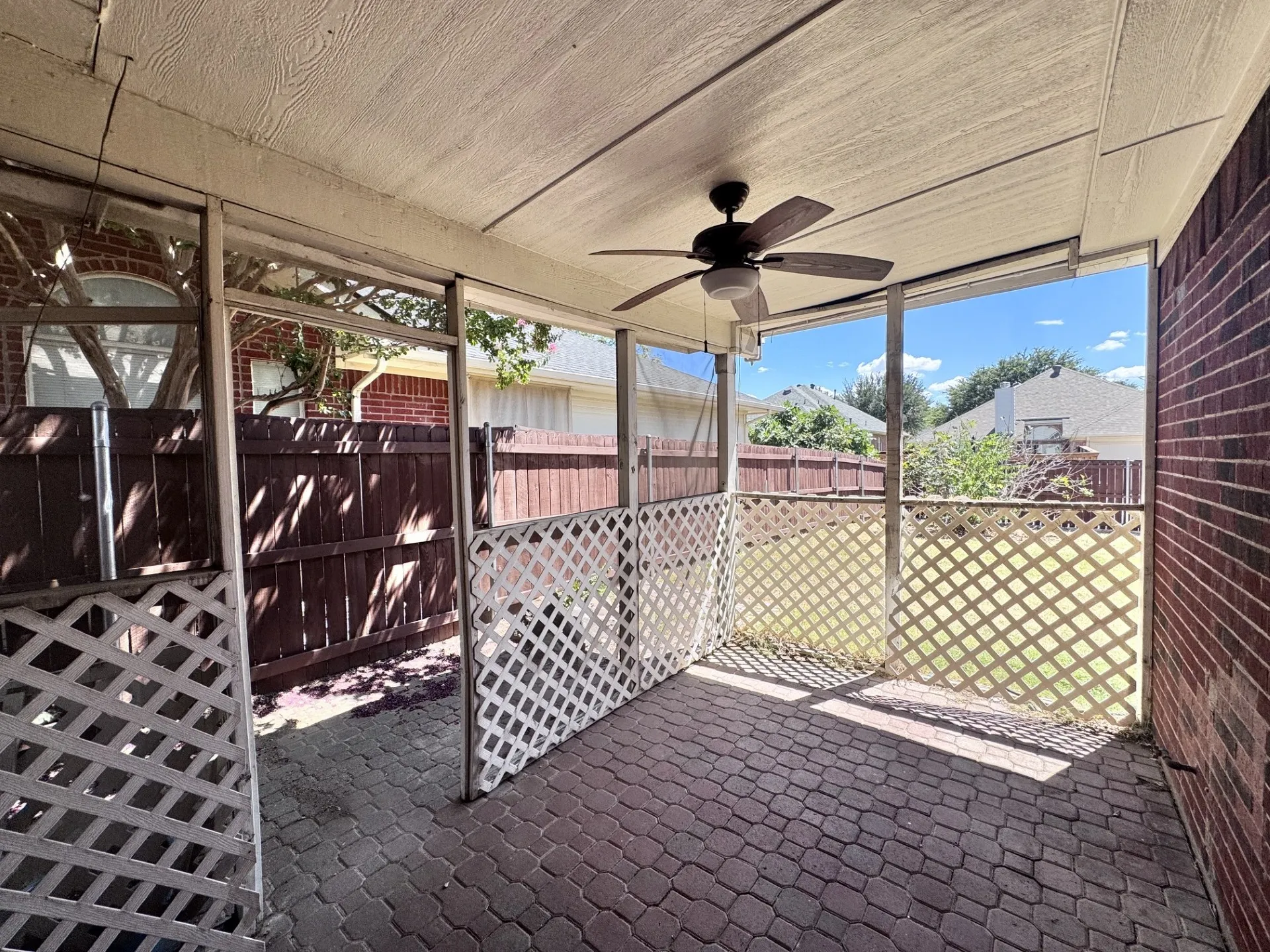Screened patio featuring a ceiling fan, brick-patterned paver flooring, and white lattice panels
