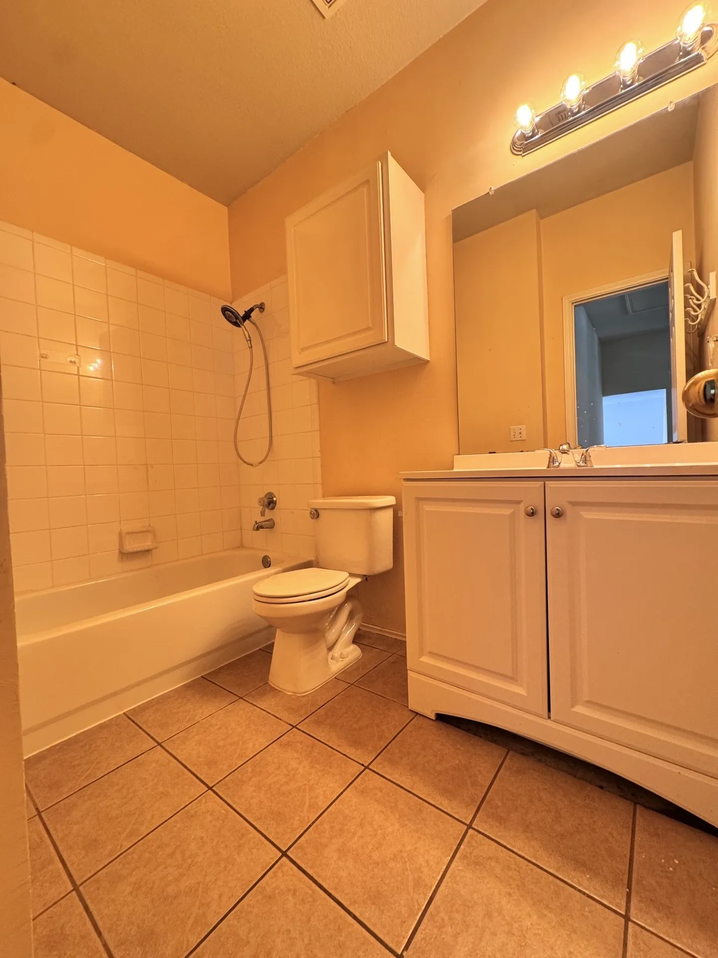 Ceramic tile flooring, white vanity with cabinet storage, white wall-mounted cabinet, tiled bathtub surround, and a four-light fixture