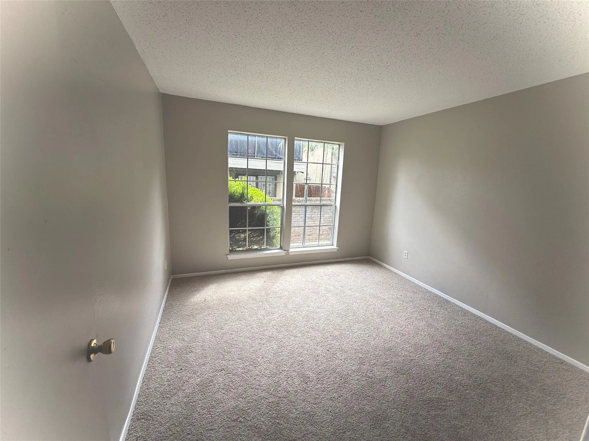 Neutral wall finishes, textured carpeting, and a window with a metal security screen