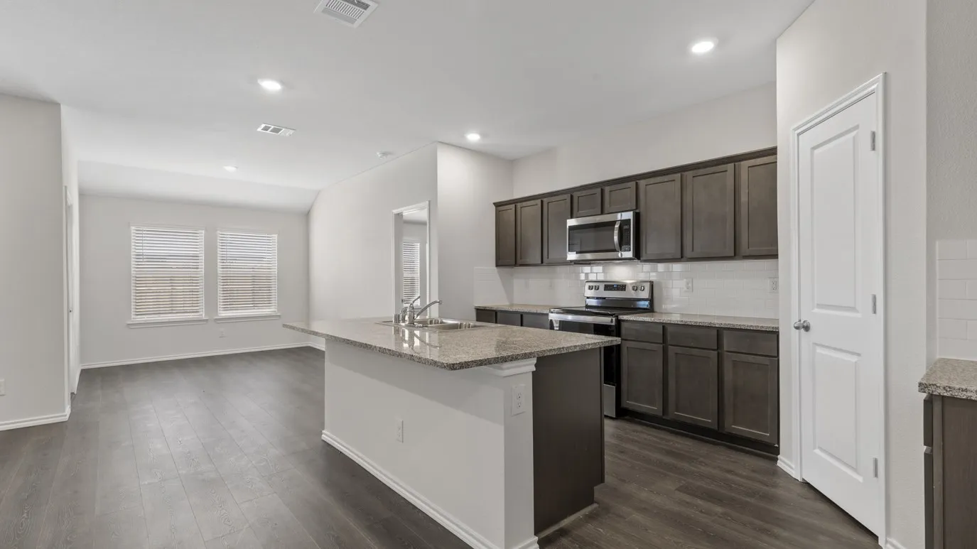 Kitchen featuring an island with a stainless steel sink, granite countertops, dark wood-finish cabinetry, stainless steel appliances, and a subway tile backsplash