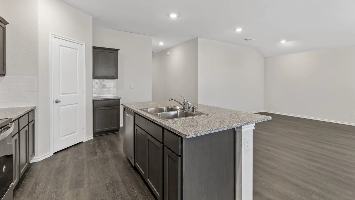 Kitchen featuring an island with a double basin sink, dark wood-finish cabinetry, light-toned countertops, and wood-finish flooring