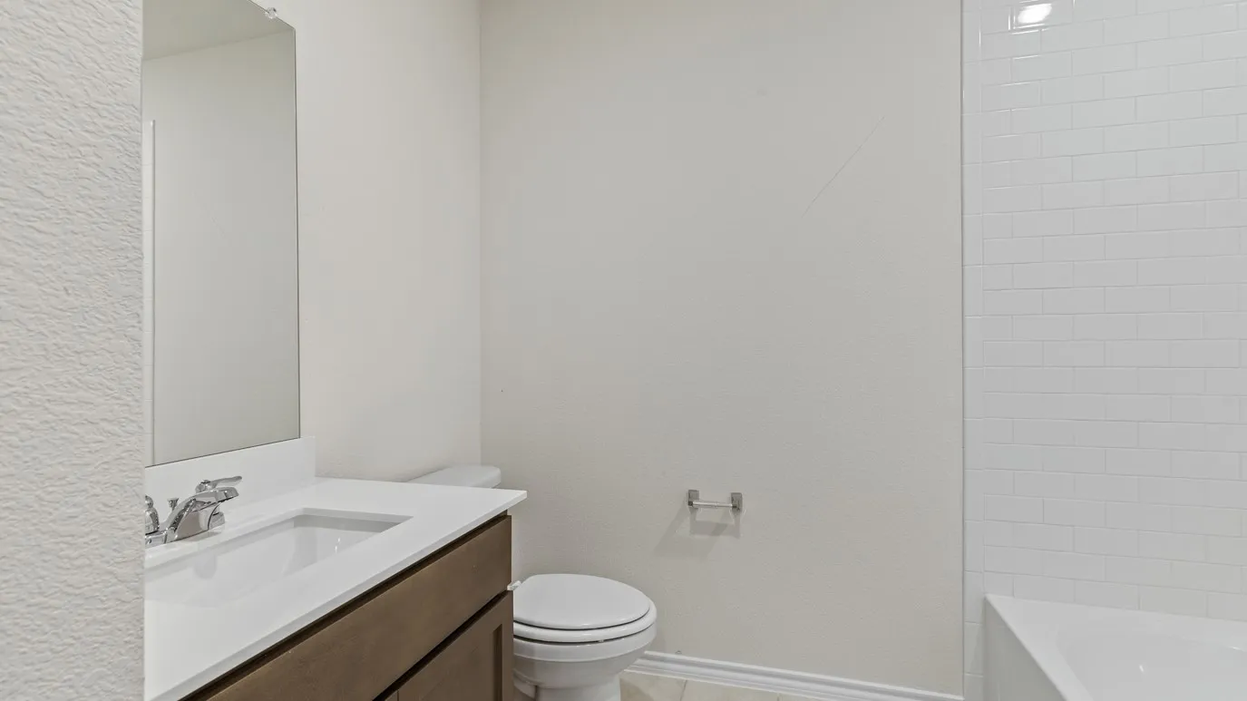 Vanity with integrated sink, chrome faucet, wall-mounted mirror, white subway tile shower surround, and a built-in bathtub