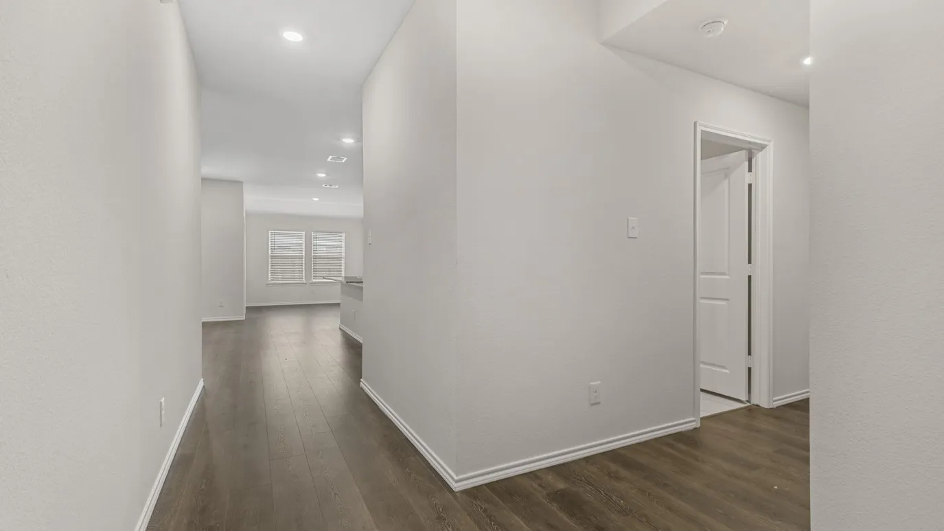 Recessed lighting illuminates the hallway with wood-finish flooring, white walls, and white trim