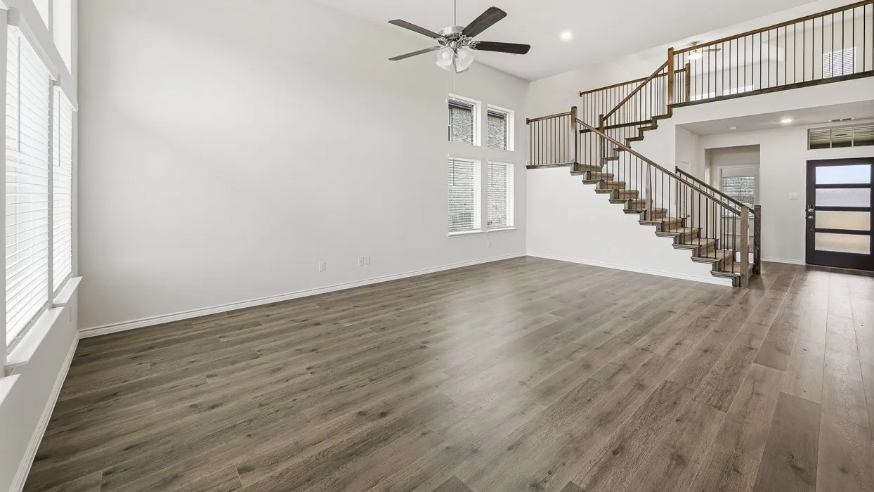 Expansive living area featuring high ceilings, wood-finish flooring, a contemporary ceiling fan, and multiple windows with blinds