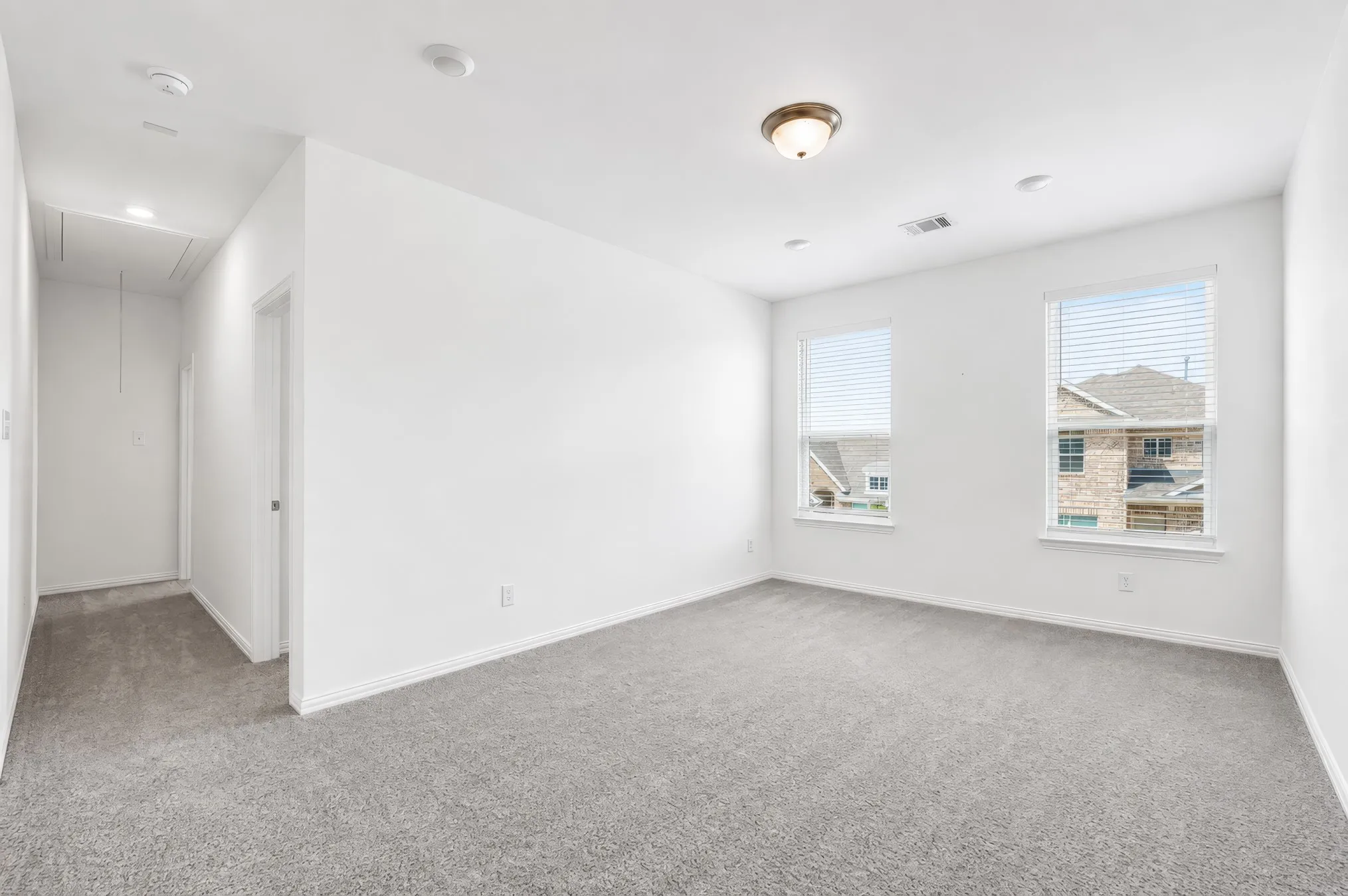 Spacious room featuring gray carpeting, white walls, two windows with blinds, recessed lighting, and a flush-mount ceiling fixture