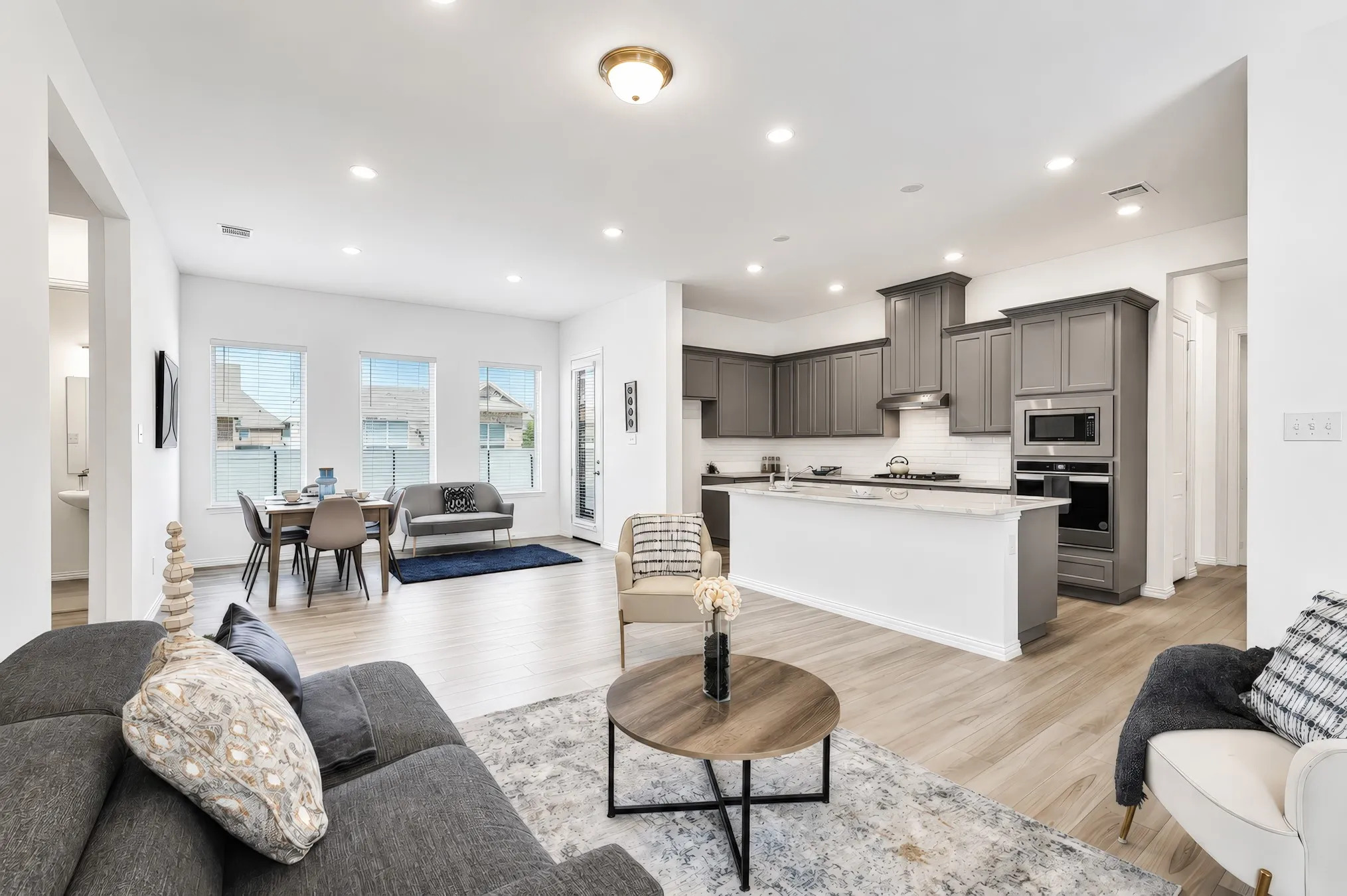 Open-concept living space with wood-finish flooring, recessed lighting, and a kitchen featuring gray cabinetry and a white subway tile backsplash