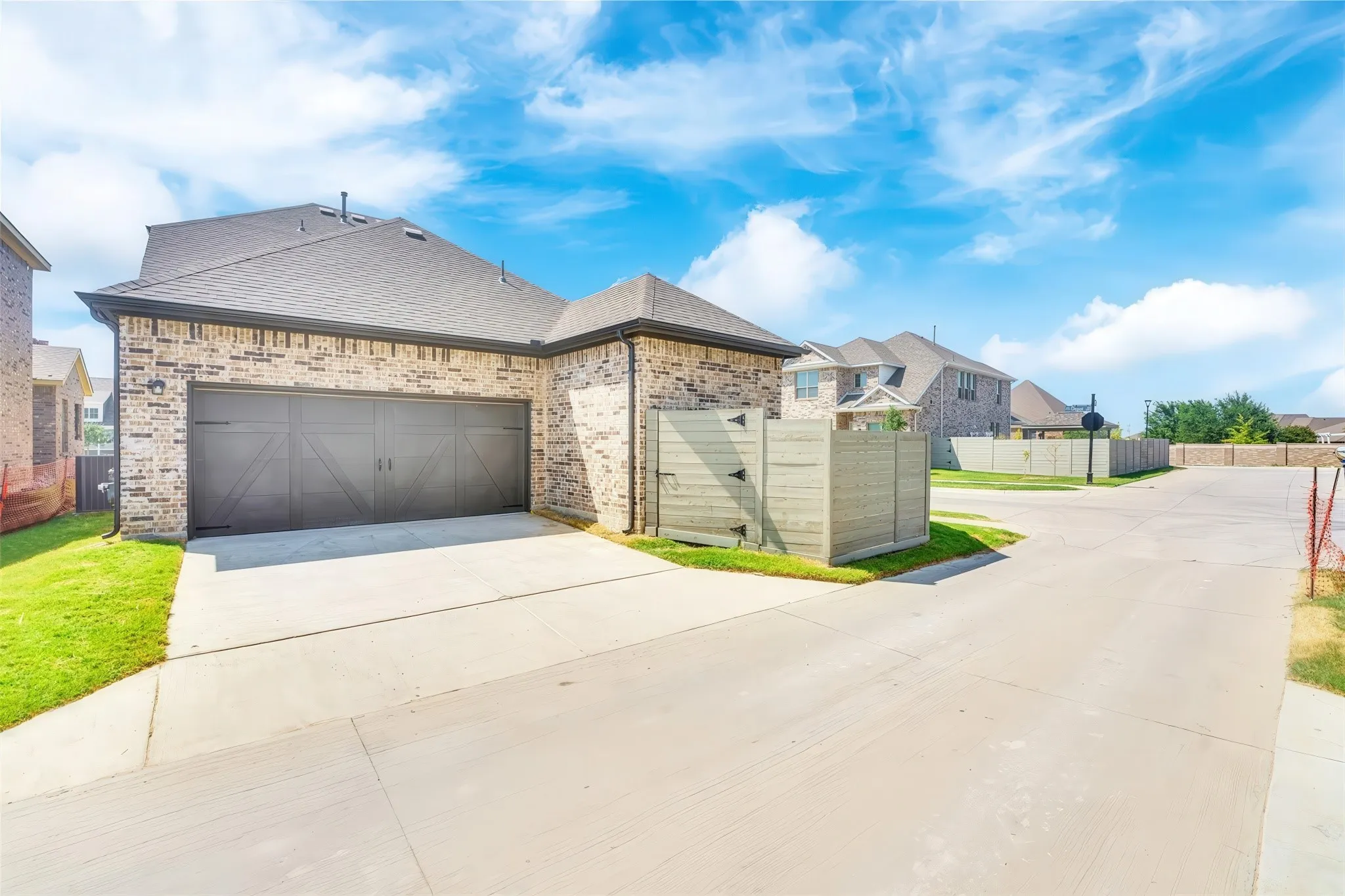 Brick exterior with a dark shingle roof, concrete driveway, and a two-car garage with barn-door style detailing