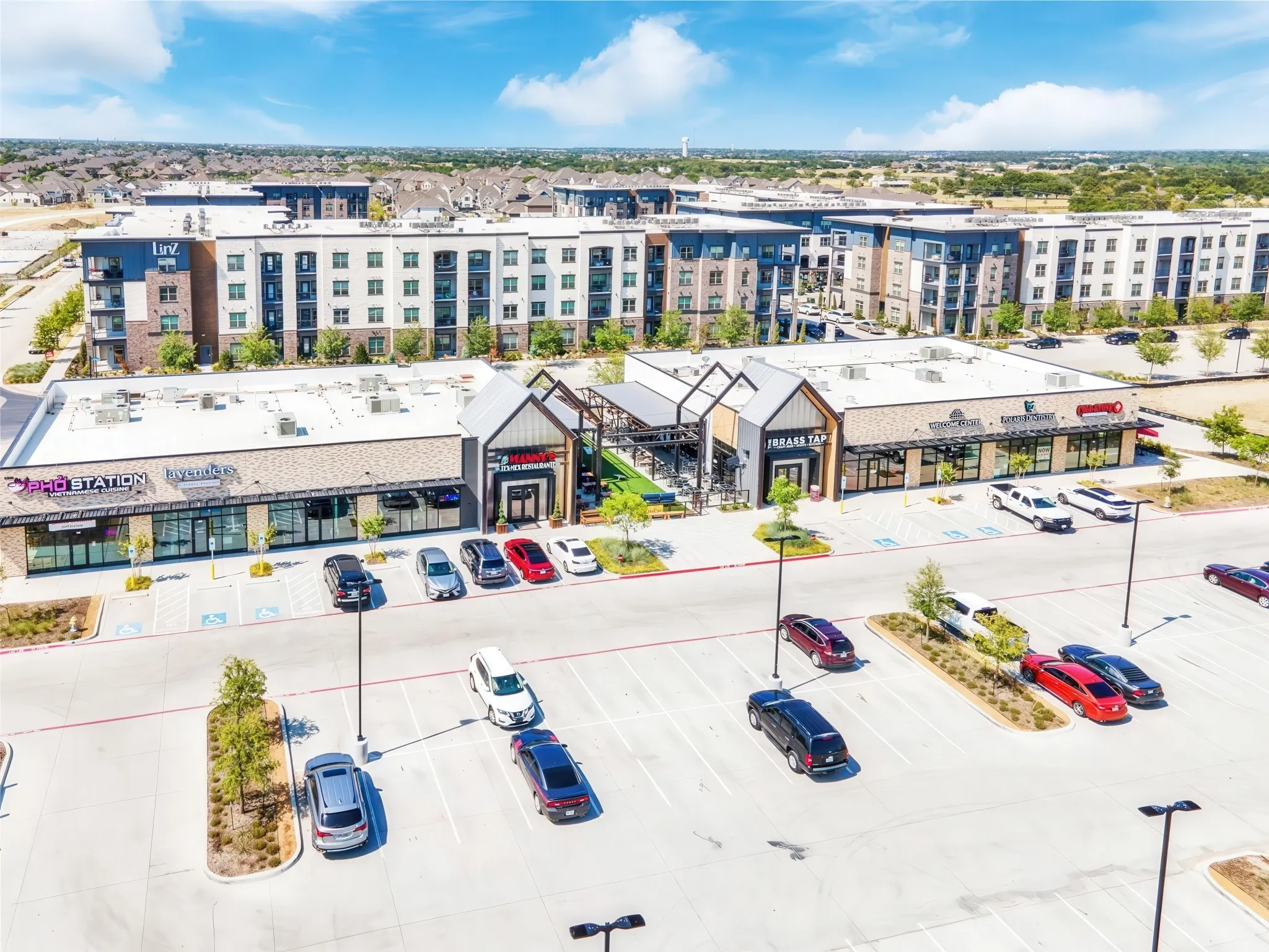 Modern commercial and residential complex featuring diverse retail spaces, multi-story residential buildings, and ample surface parking