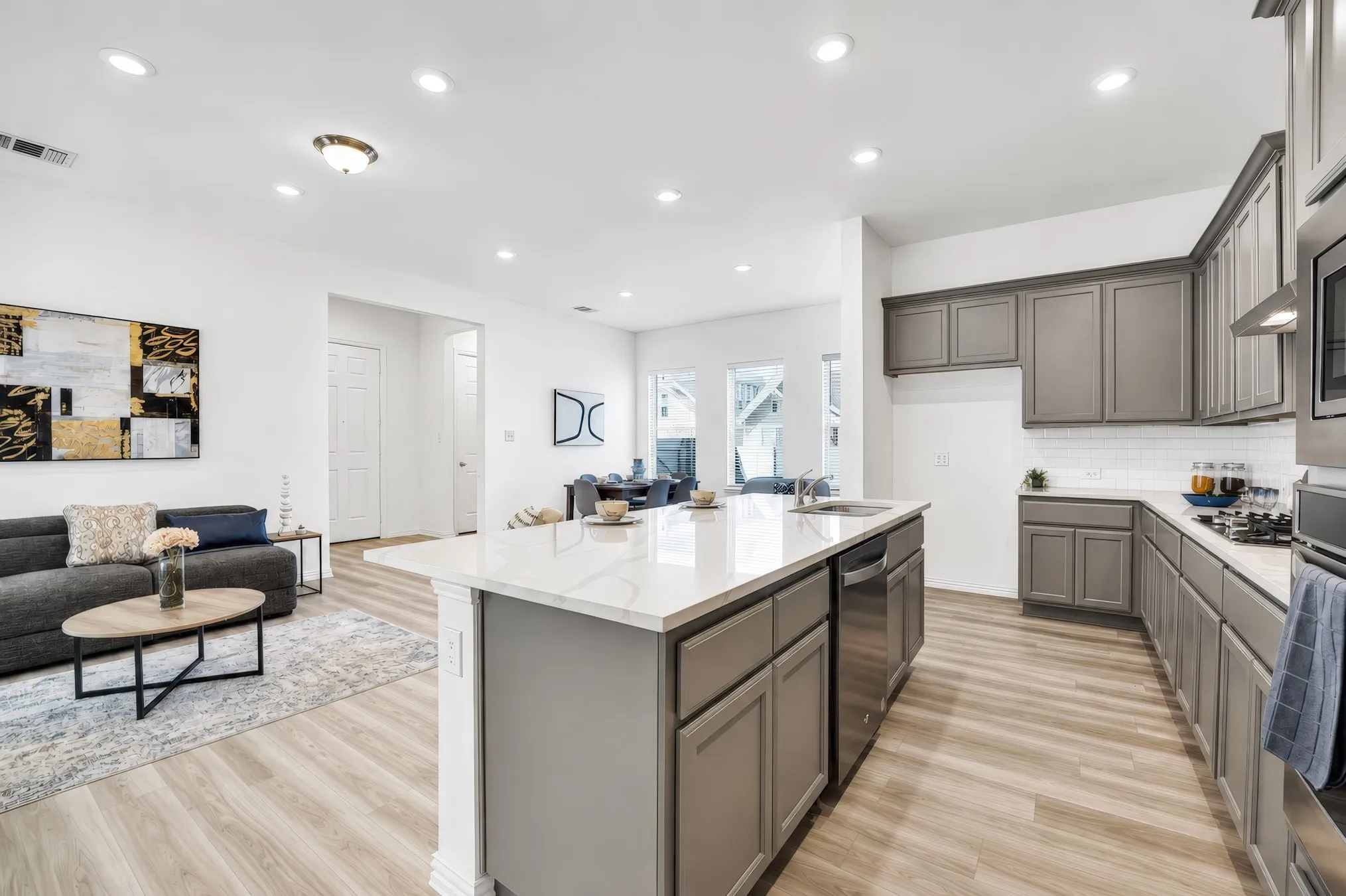 Open-concept living area featuring wood-finish flooring, a kitchen island with seating, a stainless steel dishwasher, and recessed lighting