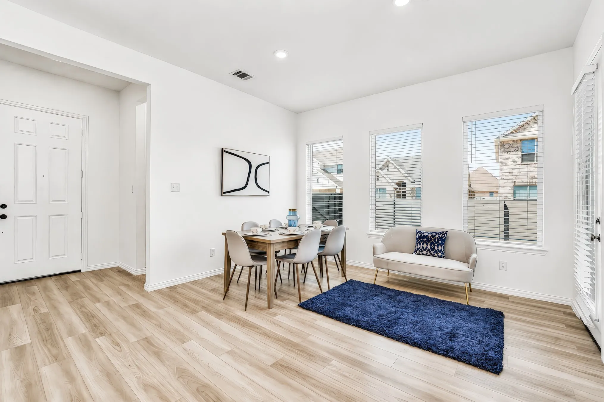 Wood-finish flooring, white paneled door, recessed lighting, multiple windows with blinds, and a white interior paint finish