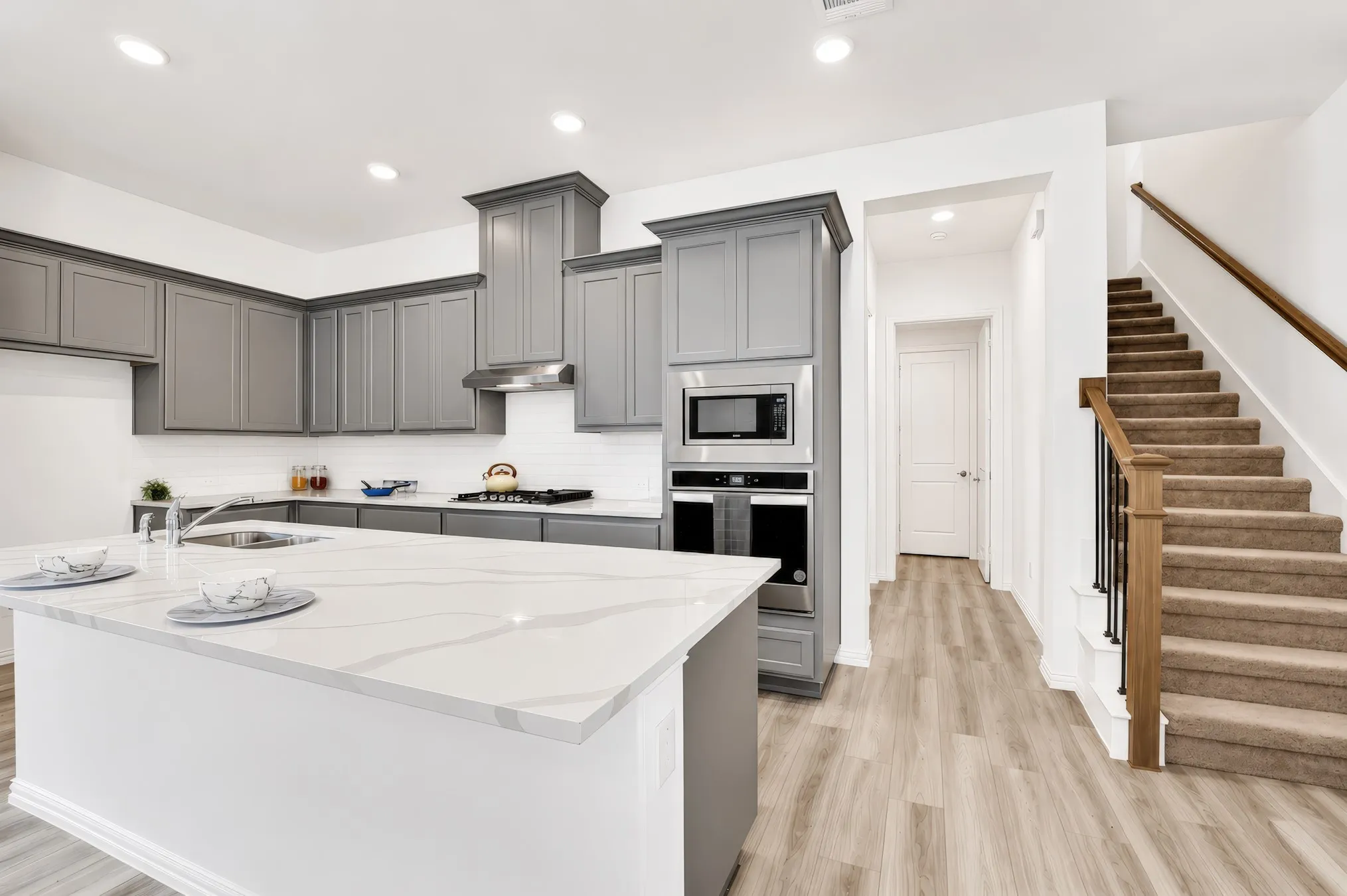 Kitchen featuring an oversized island with a stone countertop, grey shaker cabinetry, built-in stainless steel appliances, and a tile backsplash