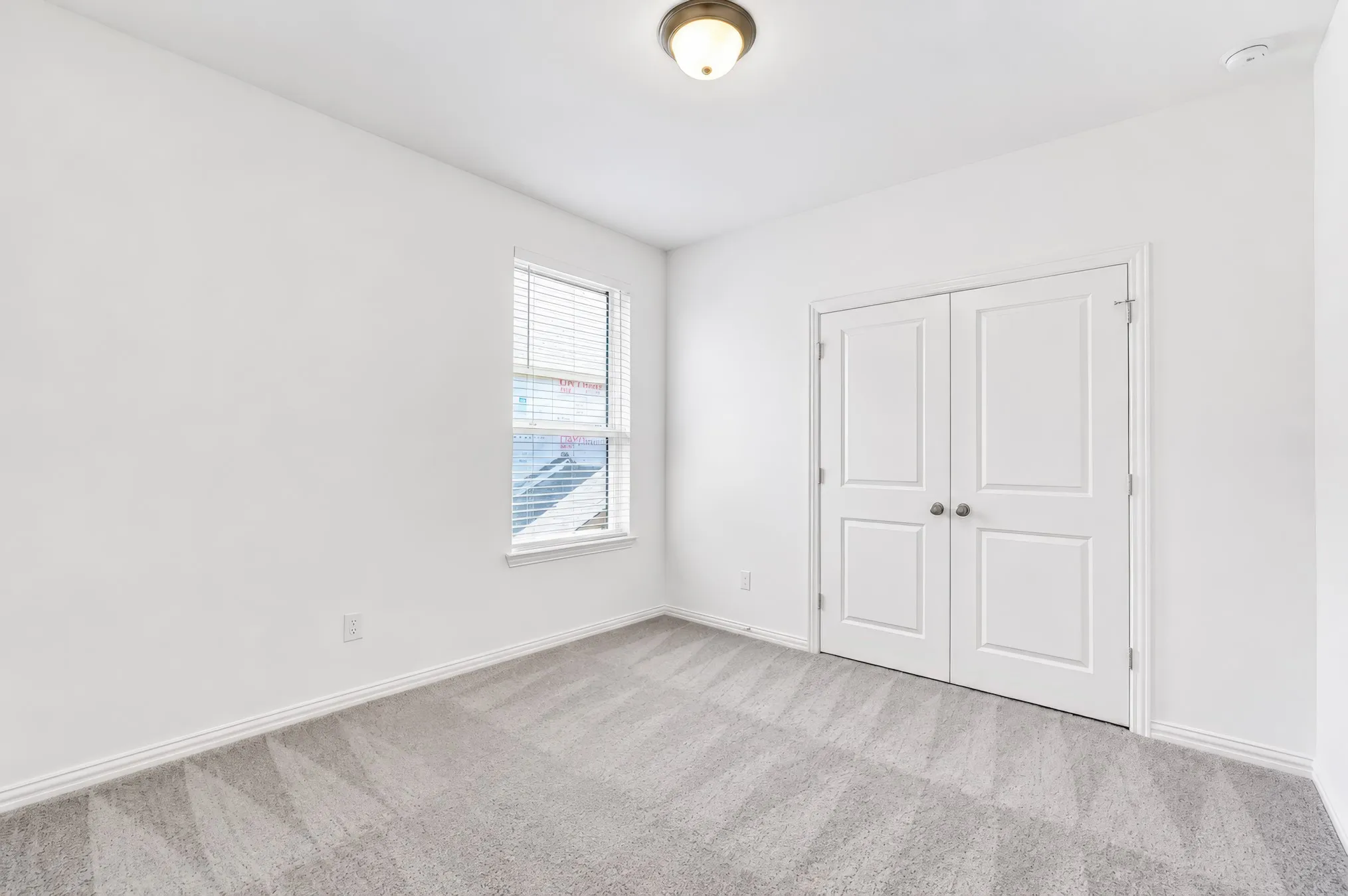 Neutral wall color, patterned carpeting, white double doors, and a single window with blinds
