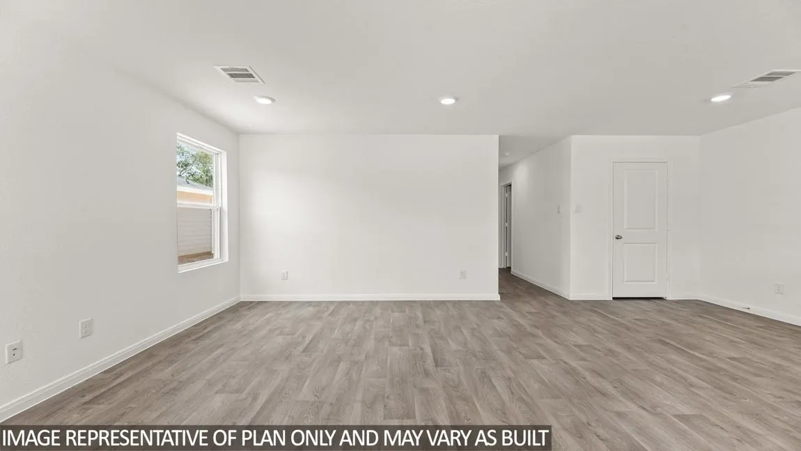 Spacious open room featuring wood-finish flooring, recessed lighting, and a white paneled door