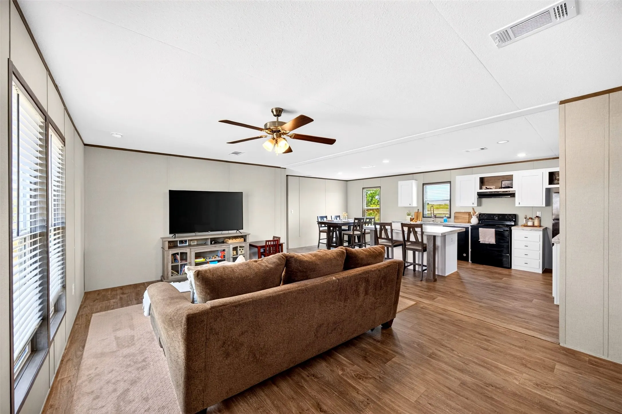 Open-concept living space featuring wood-finish flooring, white walls, and a ceiling fan
