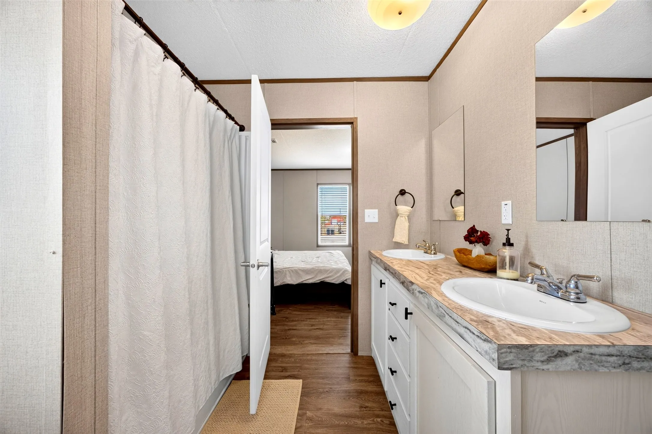 Dual vanity with integrated sinks, white cabinetry, wood-finish flooring, and a shower with a privacy curtain