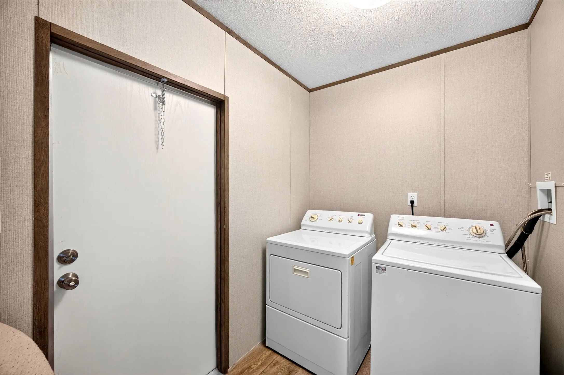 Laundry area featuring wood-finish flooring, light-toned wall panels, and a white door with wood-finish trim