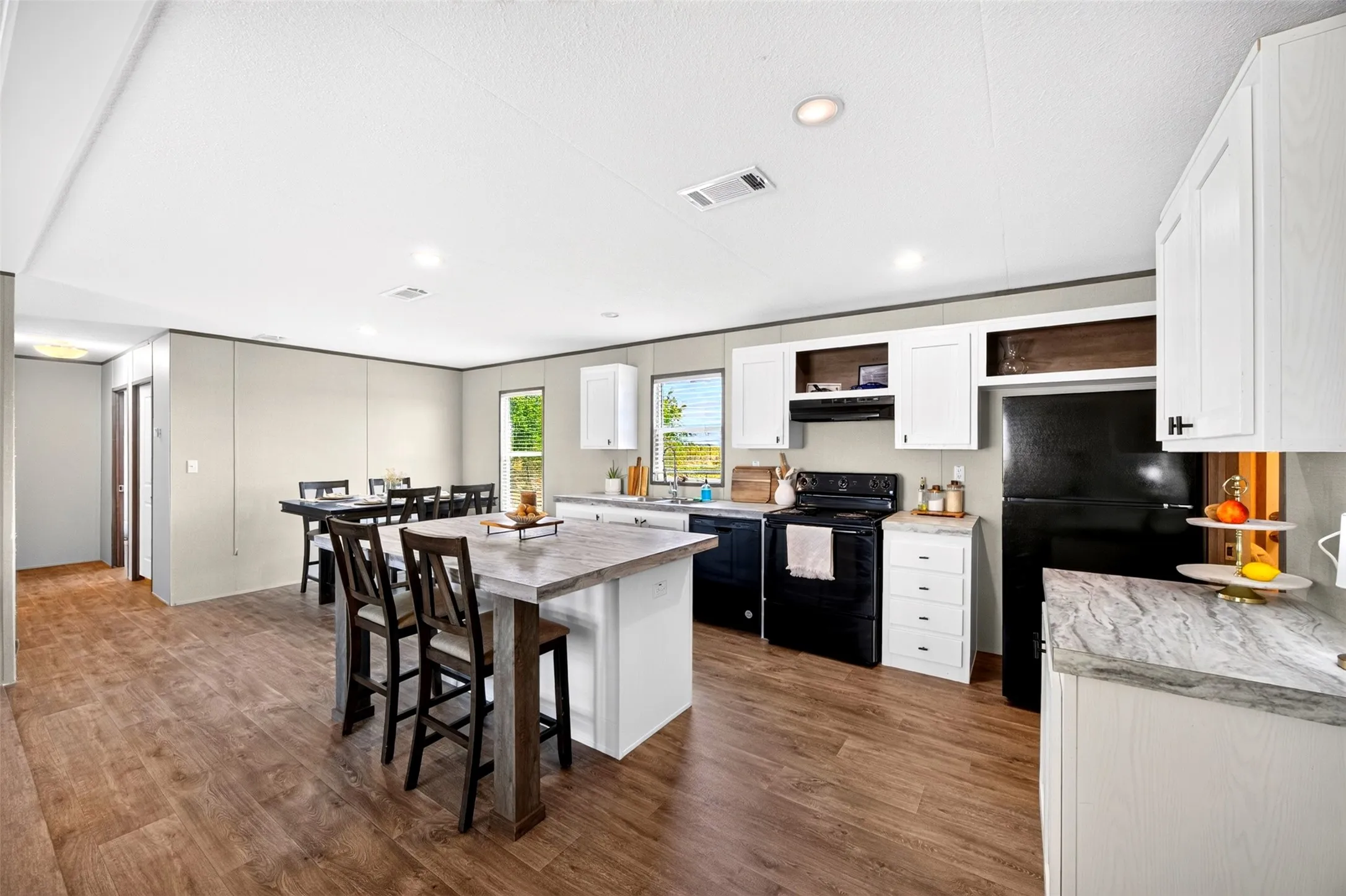 Open-concept living space with wood-finish flooring, recessed lighting, a kitchen island with seating, white cabinetry, and black appliances