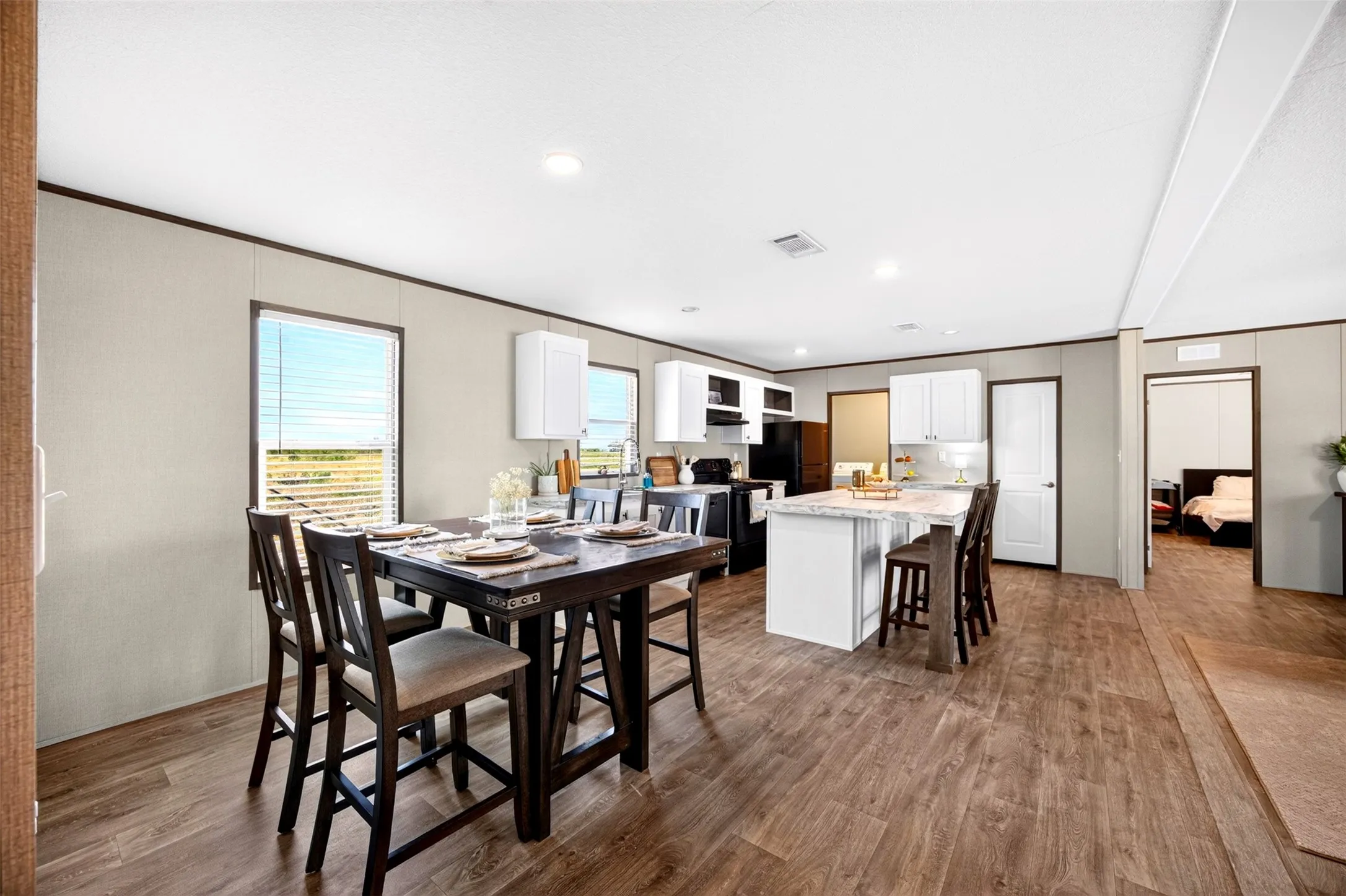 Open-concept living space featuring wood-finish flooring, white cabinetry, a kitchen island with seating, and recessed lighting