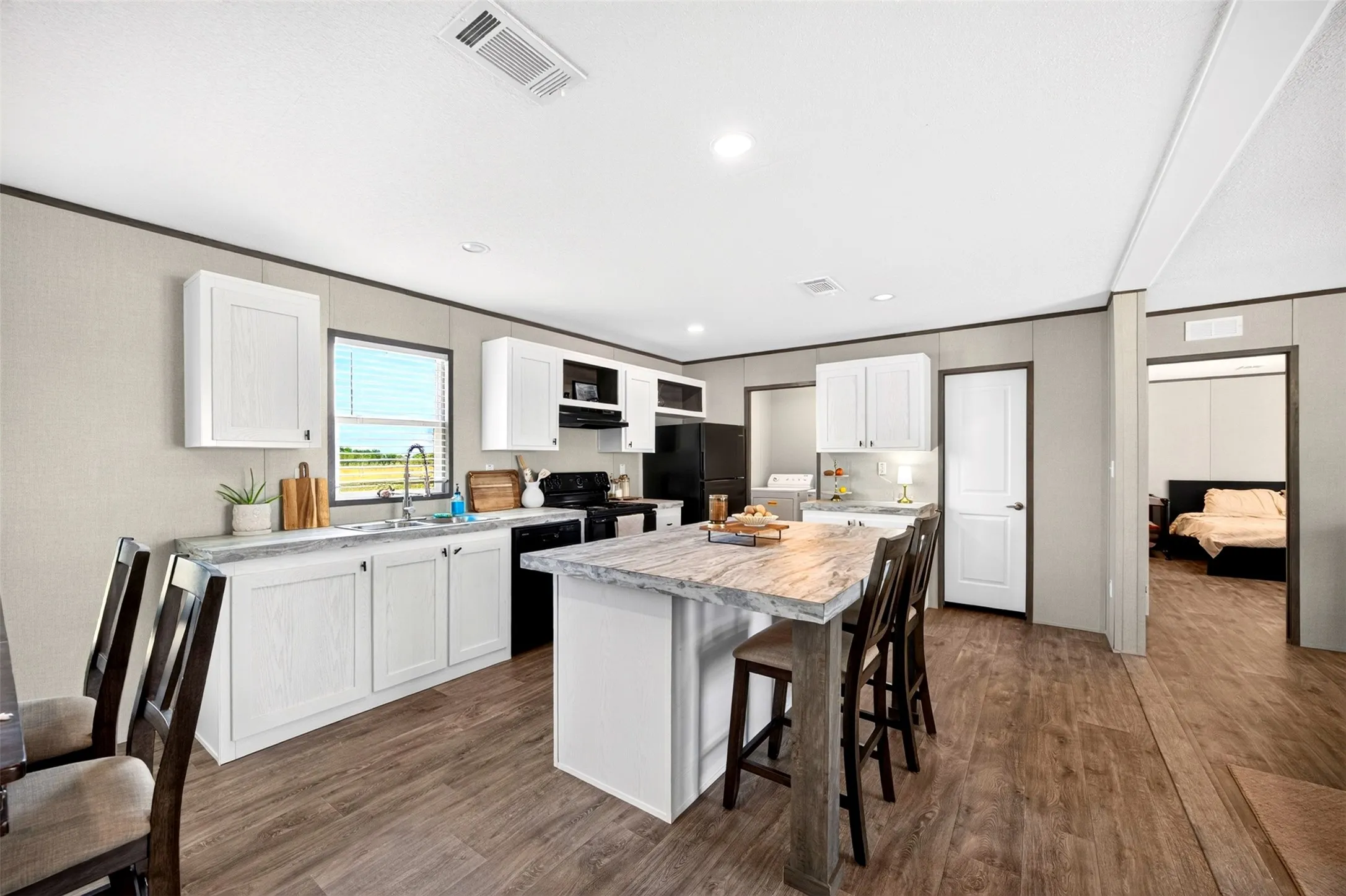 Kitchen featuring white cabinetry, dark wood-finish flooring, a kitchen island with seating, a stainless steel sink, and black appliances
