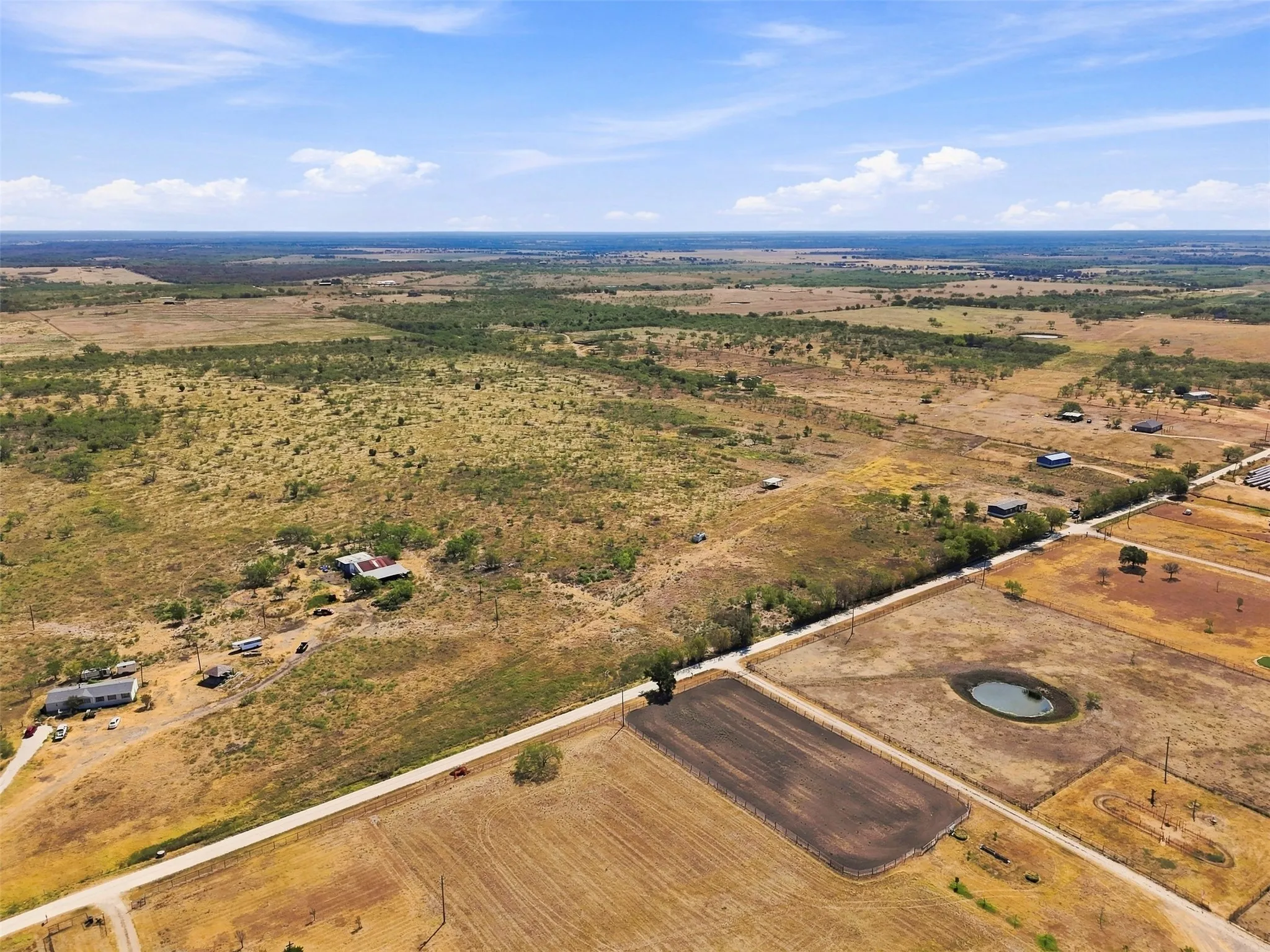 Expansive rural landscape featuring a pond, cultivated fields, and scattered residential structures