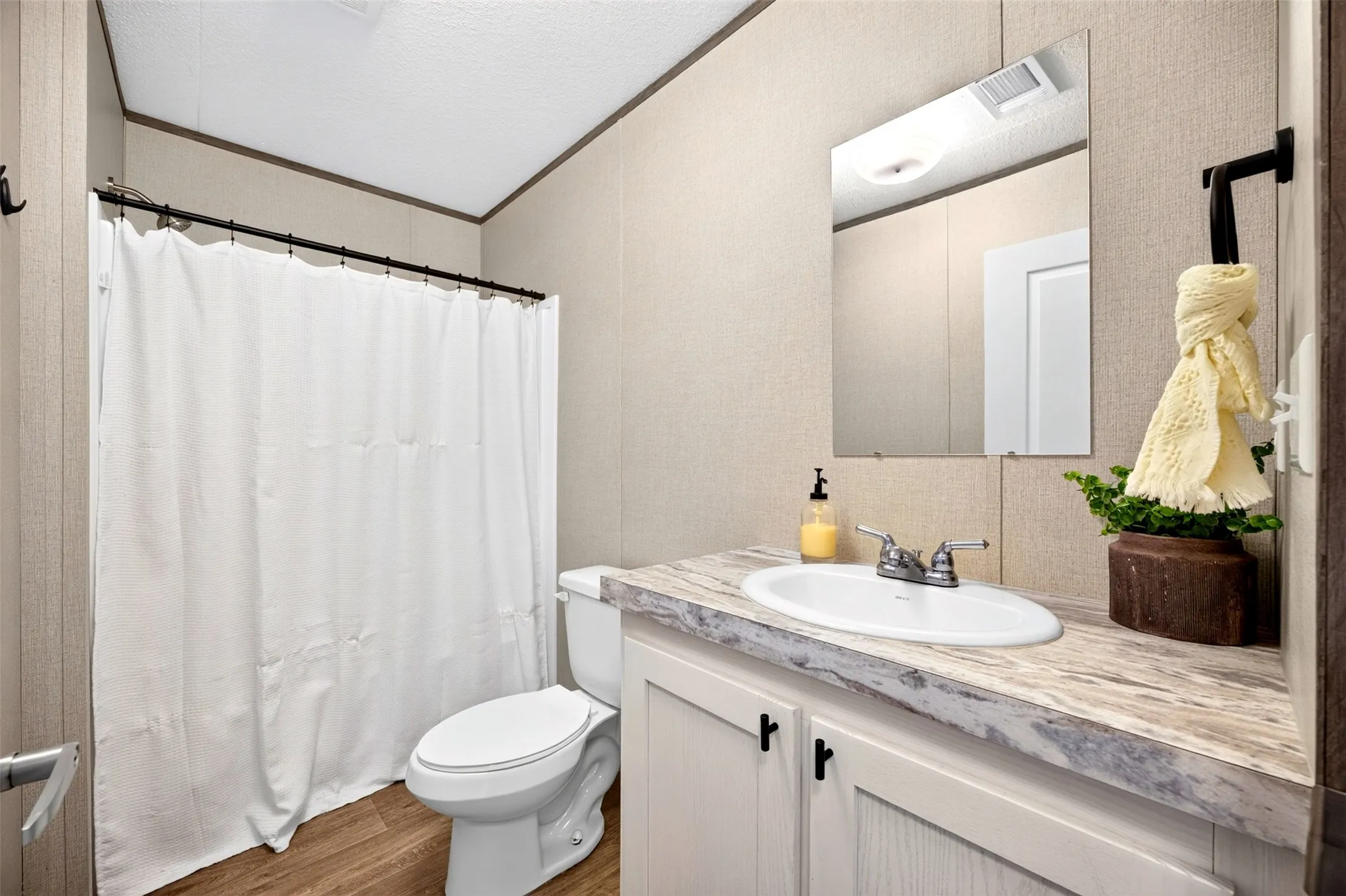 Bathroom featuring a shower with a privacy curtain, a toilet, a vanity with an integrated sink, a wall-mounted mirror, and wood-finish flooring