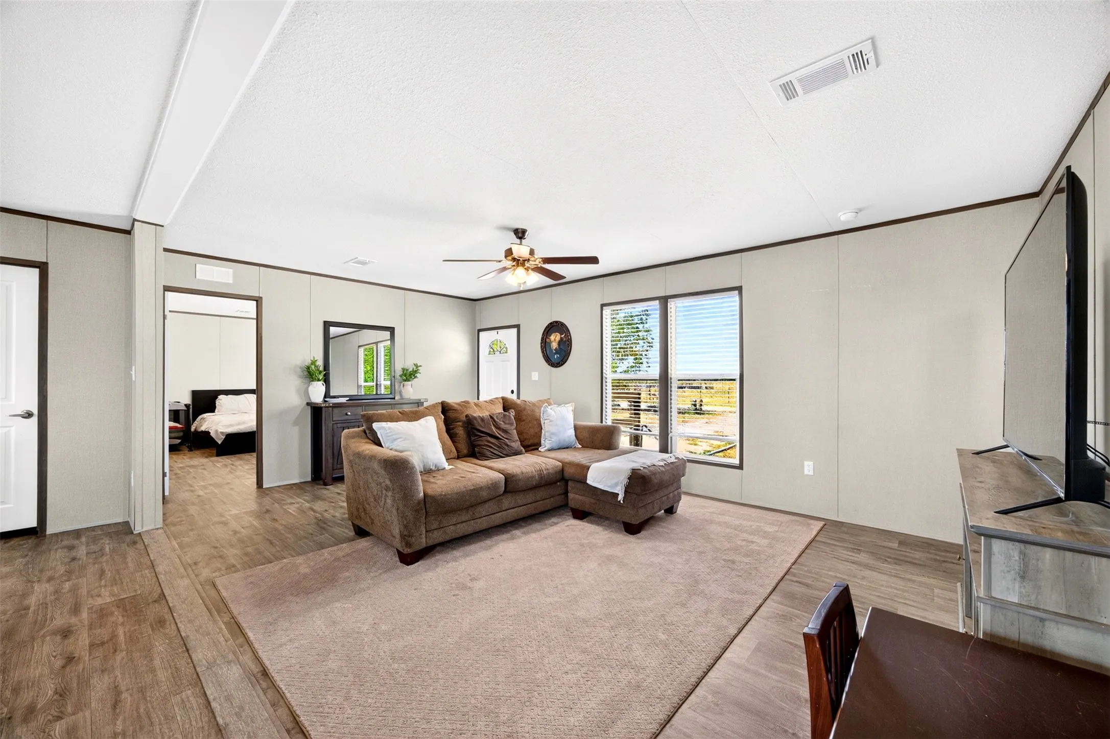 Bright living area with wood-finish flooring, light-toned walls, and a ceiling fan