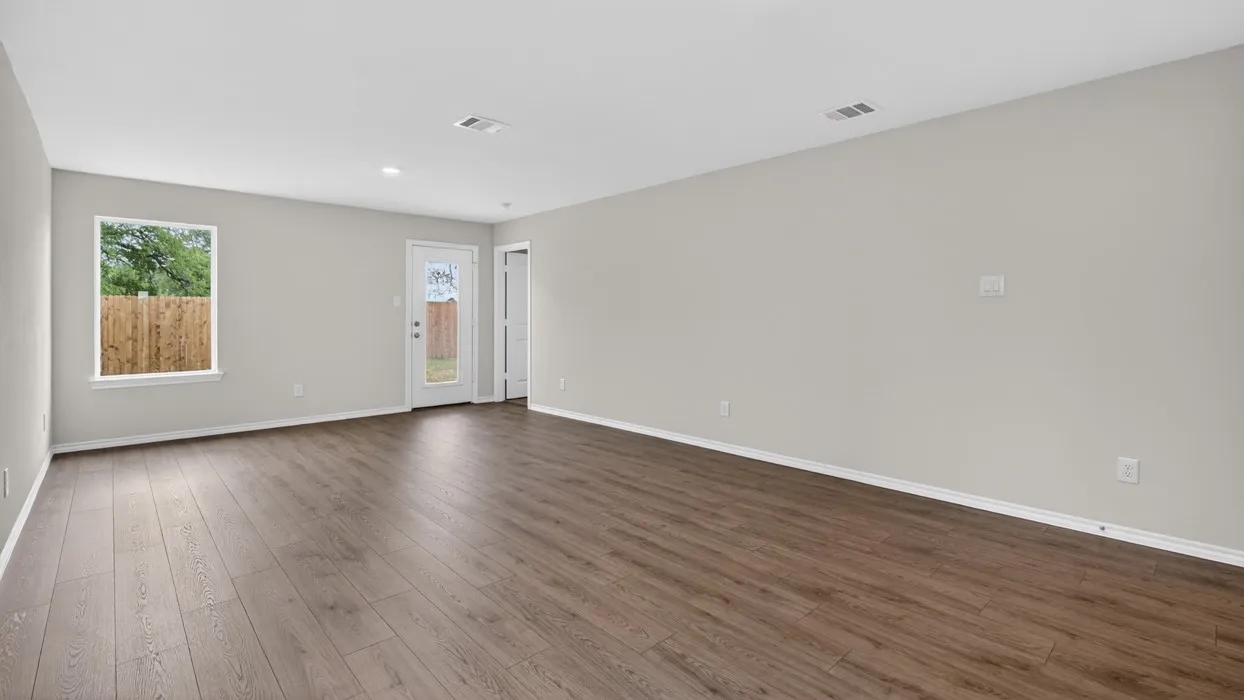 Spacious room featuring wood-finish flooring, neutral-toned walls, a bright window, and a glass-paneled door