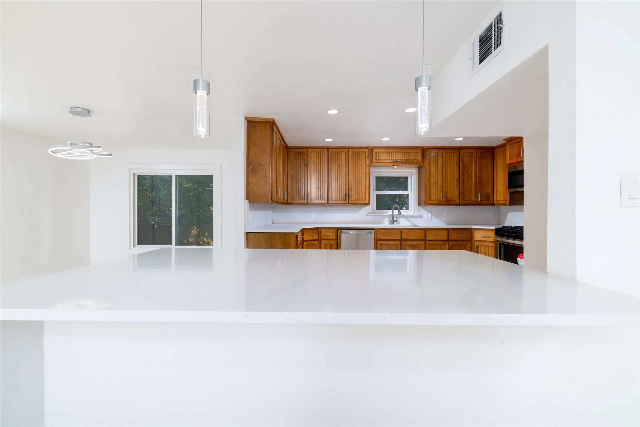 Spacious kitchen featuring white countertops, wood cabinetry, stainless steel appliances, and a sliding glass door