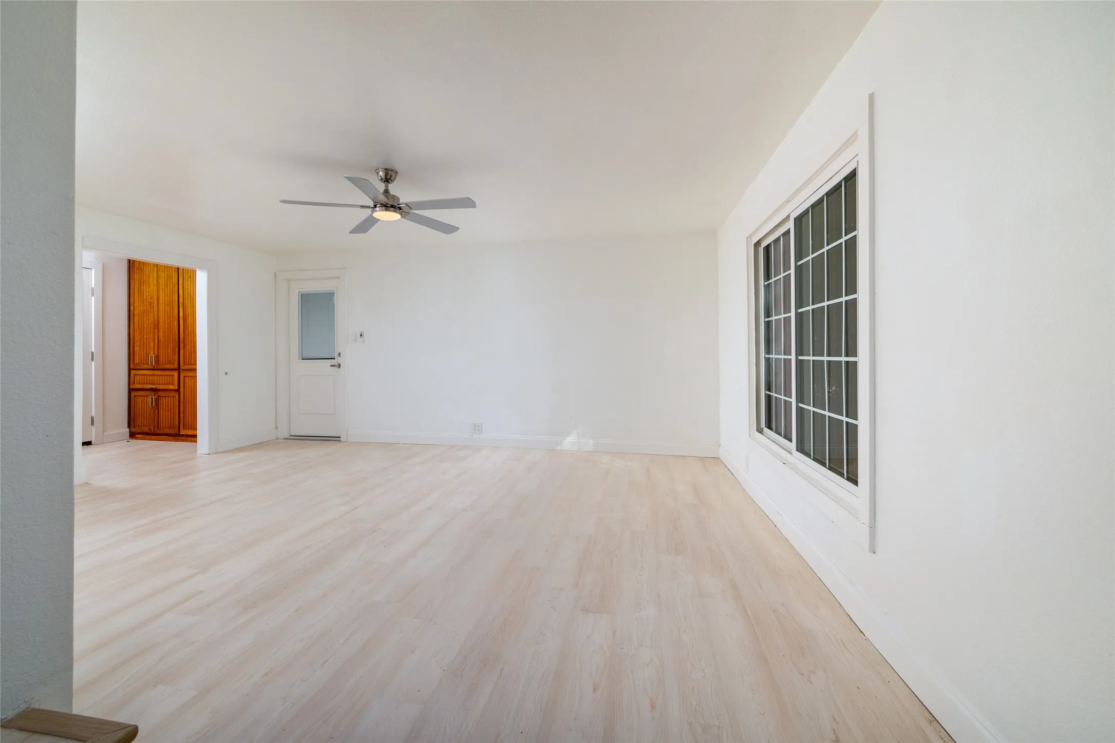 Light wood-finish flooring, white walls, and a ceiling fan with integrated lighting