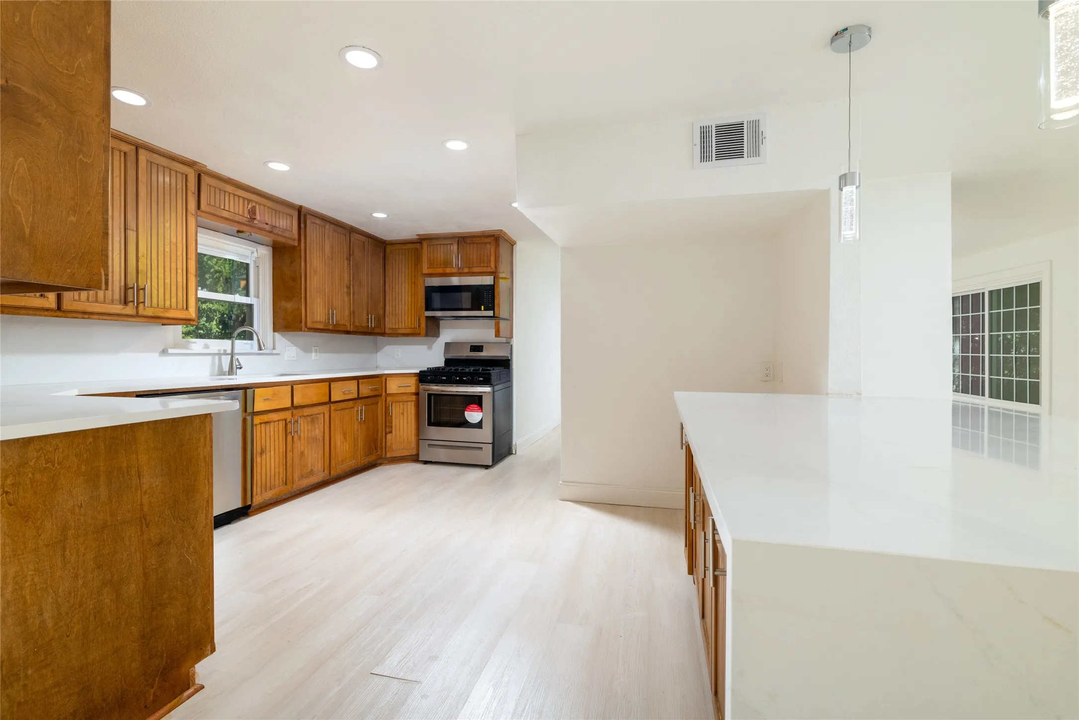 Kitchen featuring wood cabinetry, stainless steel appliances, recessed lighting, light wood-finish flooring, and white countertops