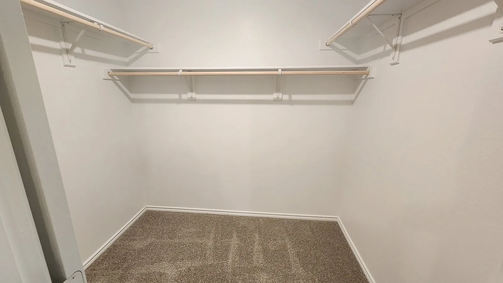Closet with two levels of shelving and hanging rods, accompanied by light-colored walls and carpeted flooring