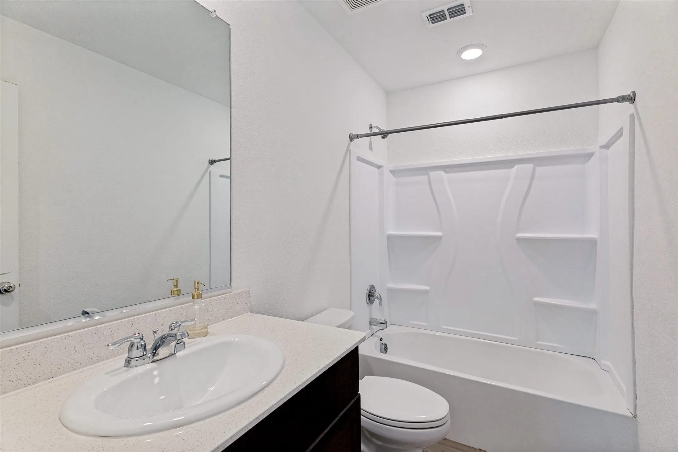 White tub/shower combination with a textured surround, single vanity with an integrated sink, polished chrome faucet, and a large wall-mounted mirror