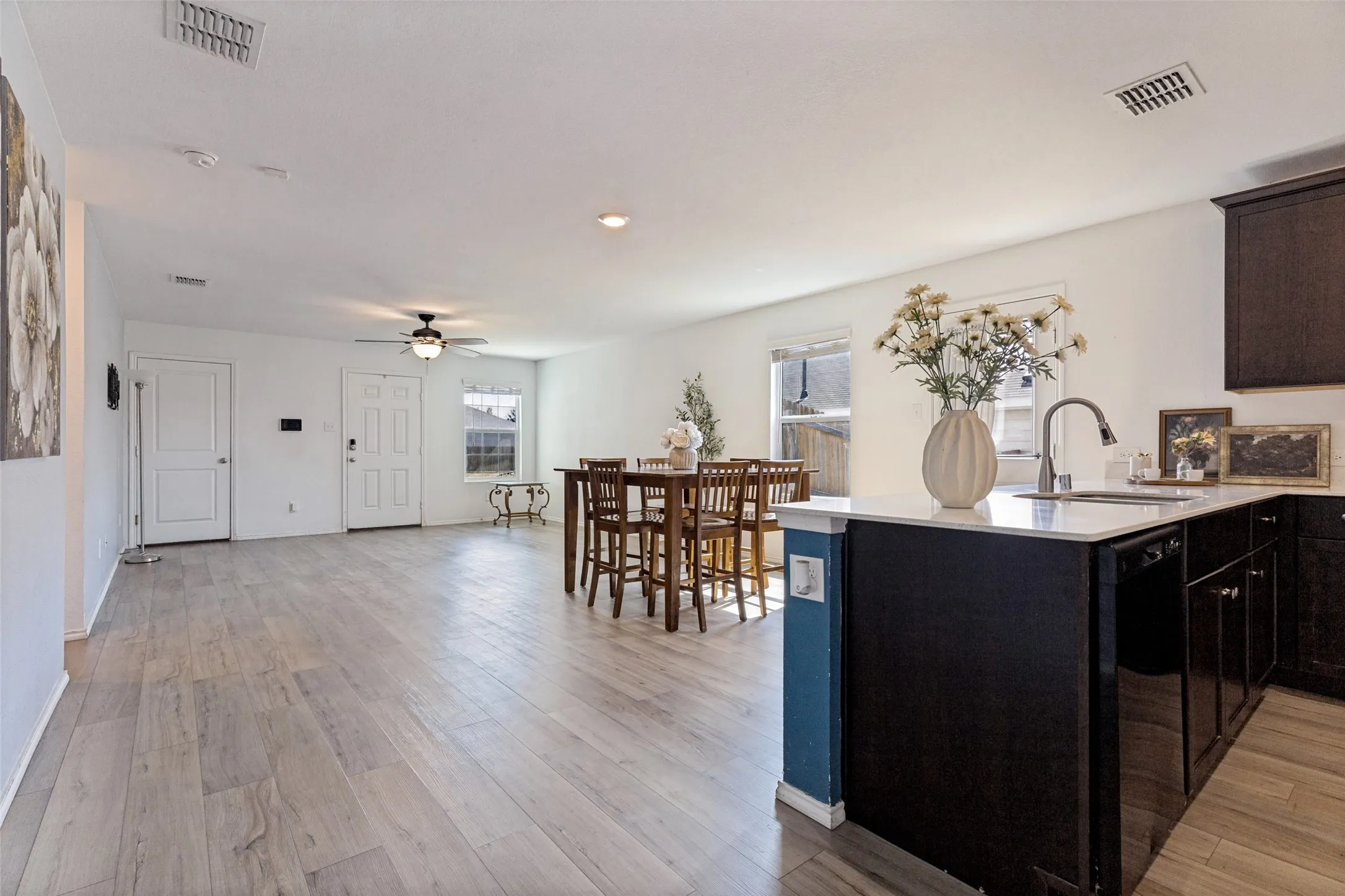 Open-concept kitchen and living area featuring a black kitchen island with blue accent paneling, stainless steel appliances, quartz countertops, and wood-finish flooring throughout