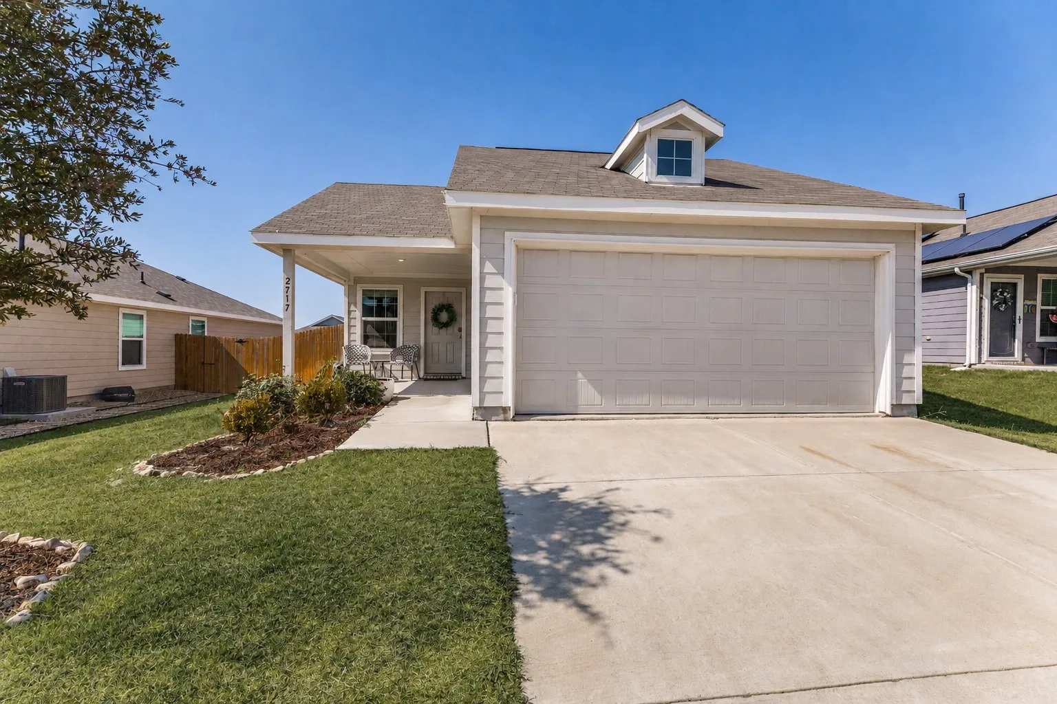 Single-story residence featuring a covered front porch, attached two-car garage, dormer window, and concrete driveway