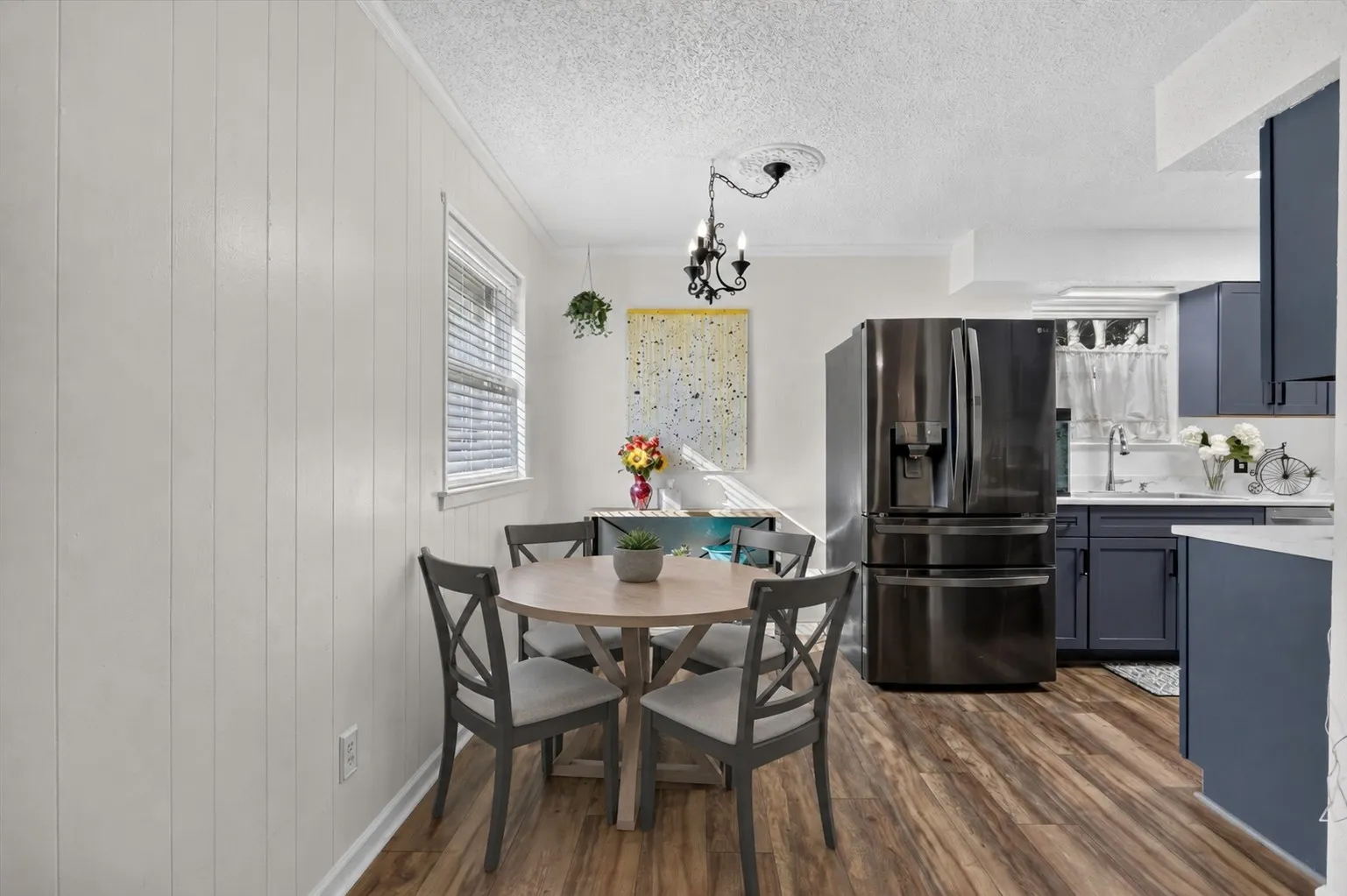 Wood-finish flooring throughout, white vertical paneling, and a window with blinds - Virtually staged with AI